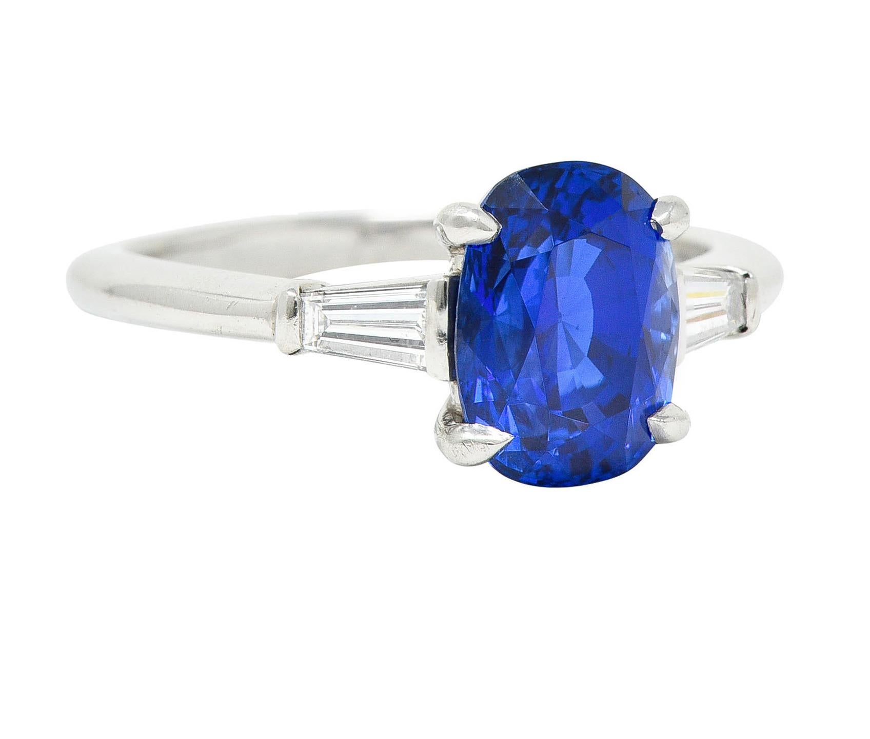 Three stone ring centers a cushion brilliant cut sapphire weighing 3.24 carats

Strongly violetish blue in color with no indications of heat - Madagascar origin

Basket set and flanked by cathedral shoulders bar set by tapered baguette cut