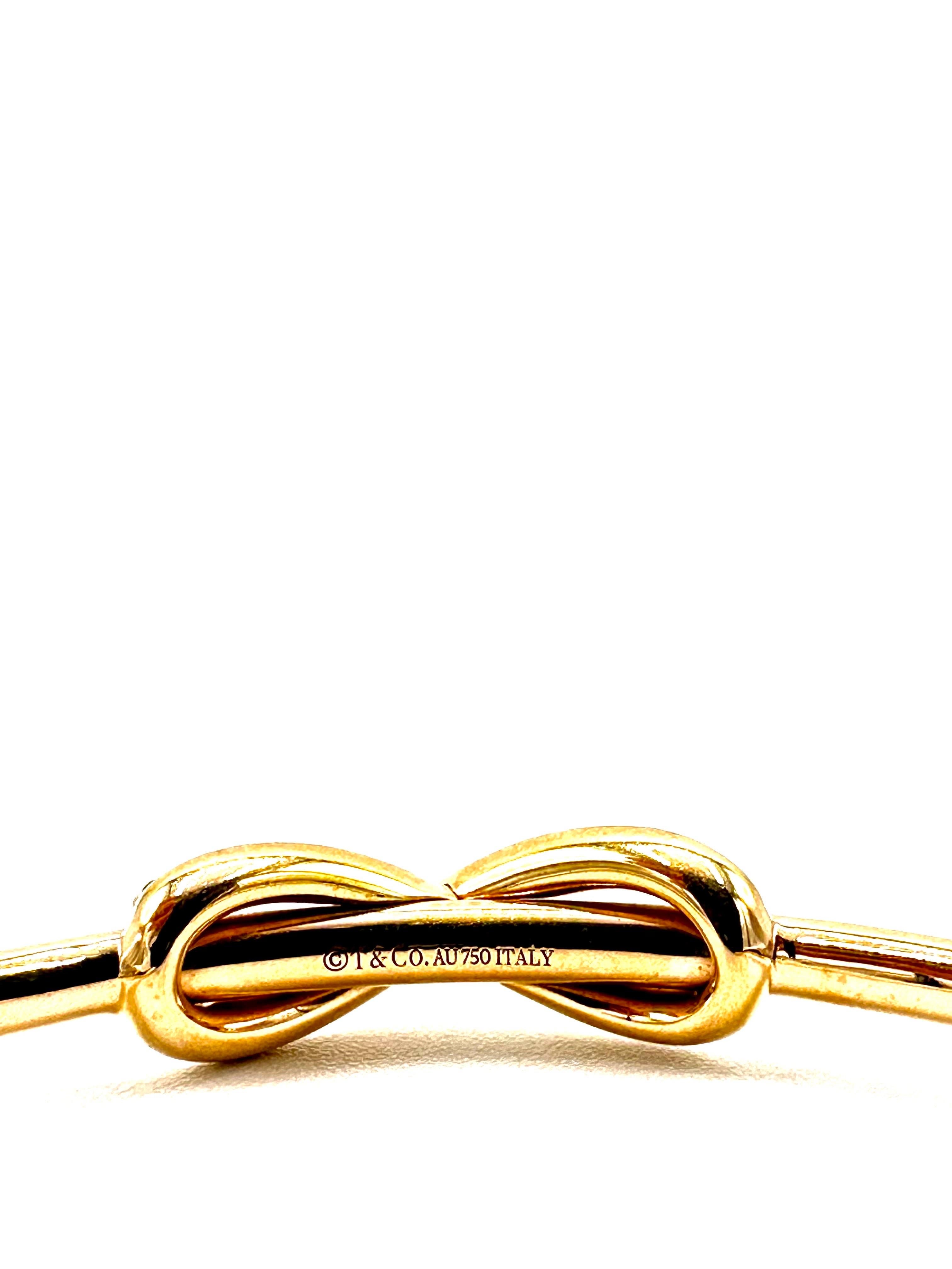 An elegant Tiffany & Co. Italy Diamond bow cuff bracelet.  The bracelet is designed with a round brilliant Diamond figure eight in the center on a three millimeter solid gold round cuff, with a single row of Diamonds around each end at the opening. 