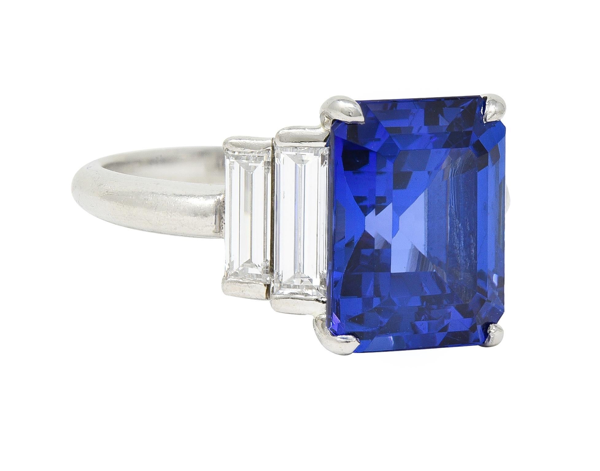 Centering an emerald cut tanzanite weighing 6.42 carats total - transparent medium violetish blue 
Prong set in basket and flanked by stepped shoulders bar set with baguette cut diamonds 
Weighing 1.50 carats total - E/F color with VS1 clarity