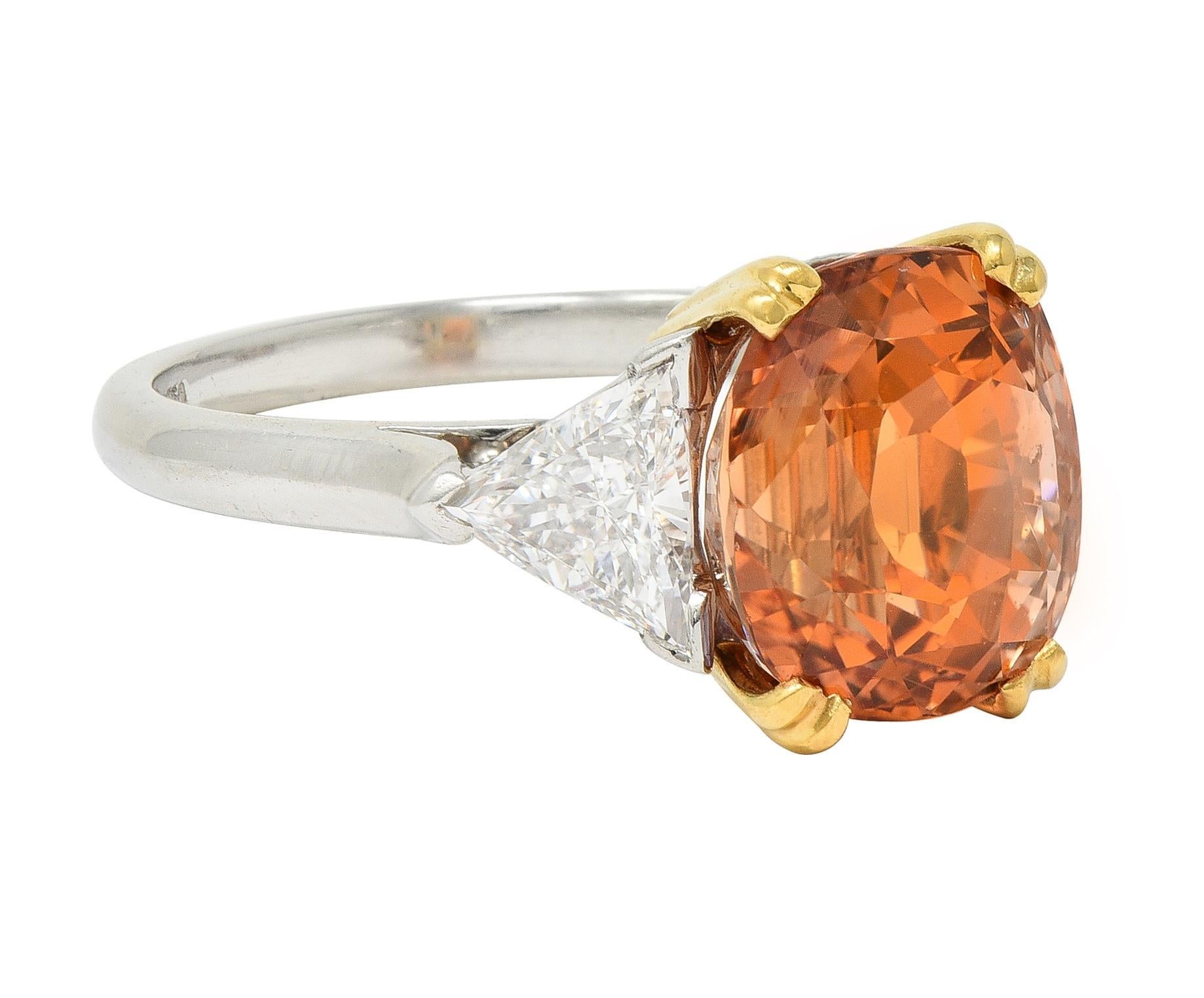 Centering a cushion cut sapphire weighing approximately 7.66 carats - transparent light pinkish-orange 
Set with split gold prongs in basket mount and flanked by cathedral shoulders
Bar set with trilliant cut diamonds weighing approximately 0.95