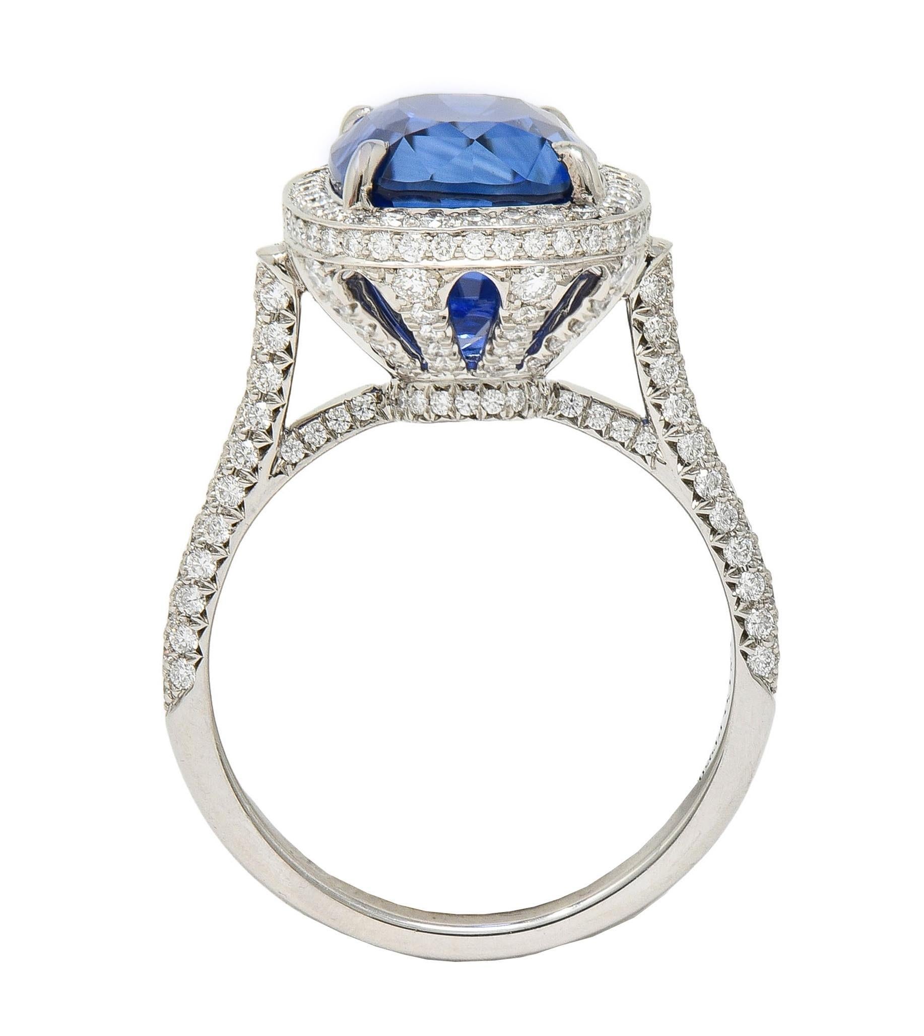 Centering an elongated cushion cut sapphire weighing approximately 8.04 carats 
Natural Madagascar in origin - transparent medium royal blue in color 
Set with talon prongs in a pierced foliate basket with halo surround
Featuring round brilliant cut