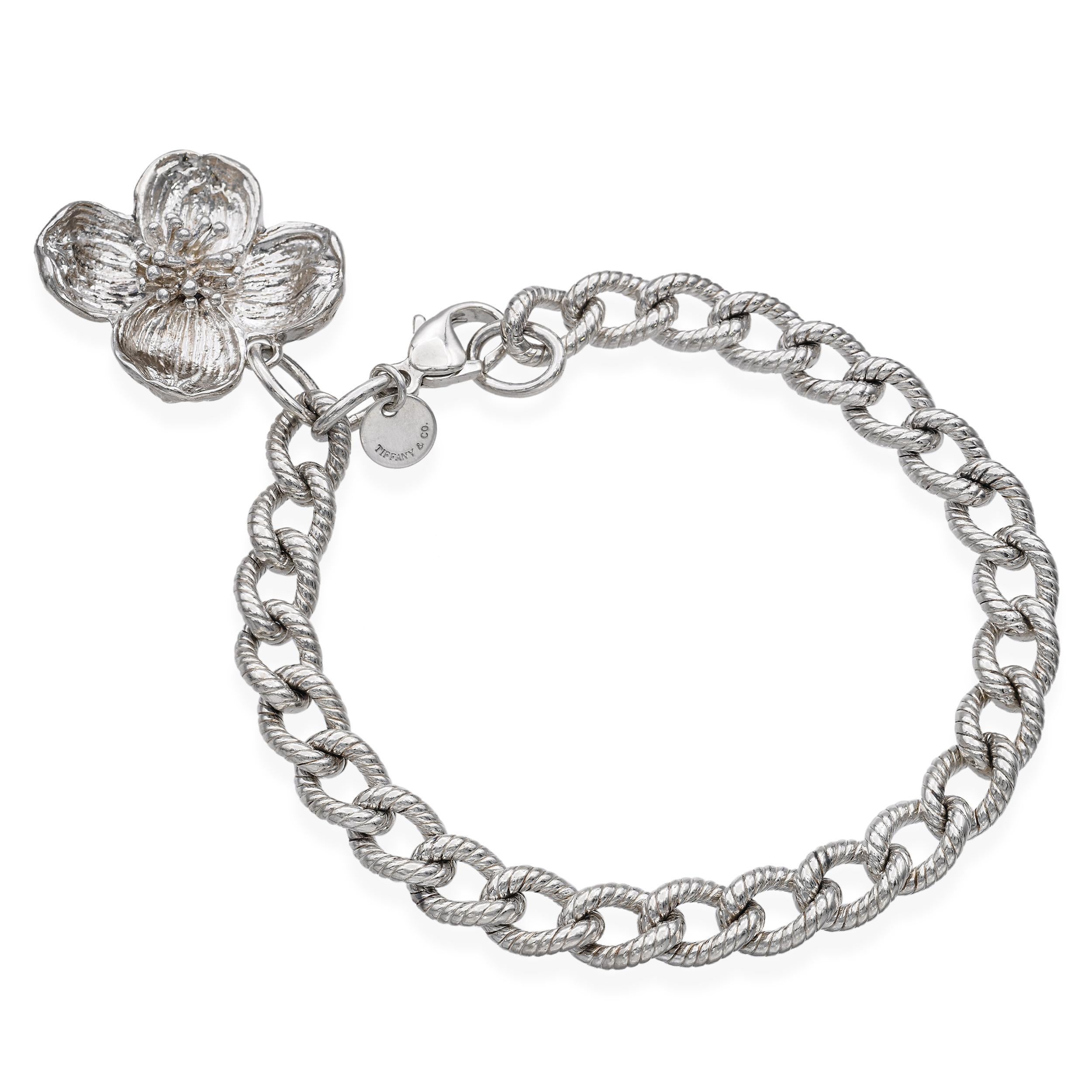 This elegant bracelet by Tiffany & Co. is crafted in 925 sterling silver and adorned with delicate dogwood flower charms. Each charm is finely detailed, capturing the natural beauty of the blossoms with Tiffany’s signature craftsmanship. The