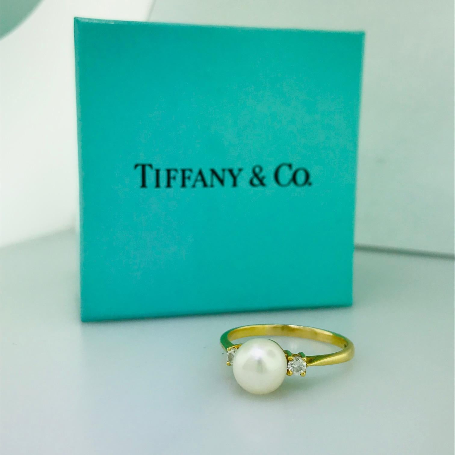 This Tiffany & Company pearl and diamond ring is an original Tiffany & Co. piece. The 18 karat yellow gold ring has one round Akoya pearl in the center with two round brilliant diamonds on either sides. The side diamonds are .10 carat total diamond