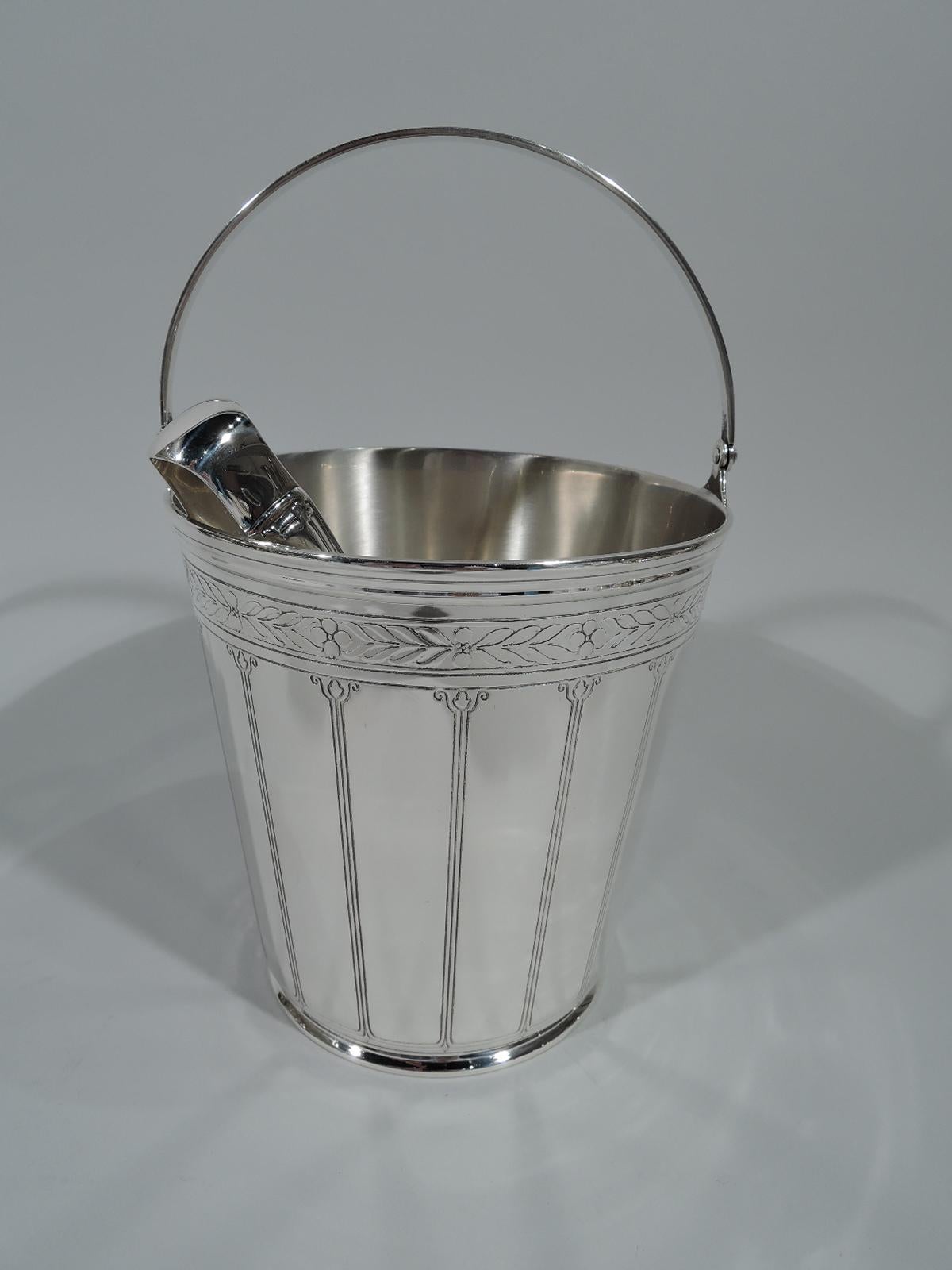 Art Deco sterling silver ice bucket. Made by Tiffany & Co. in New York. Straight and tapering sides and tapering C-scroll swing handle. Engraved and acid-etched stylized ornament. Exterior has imbricate leaf-and-berry band and volute colonnade.