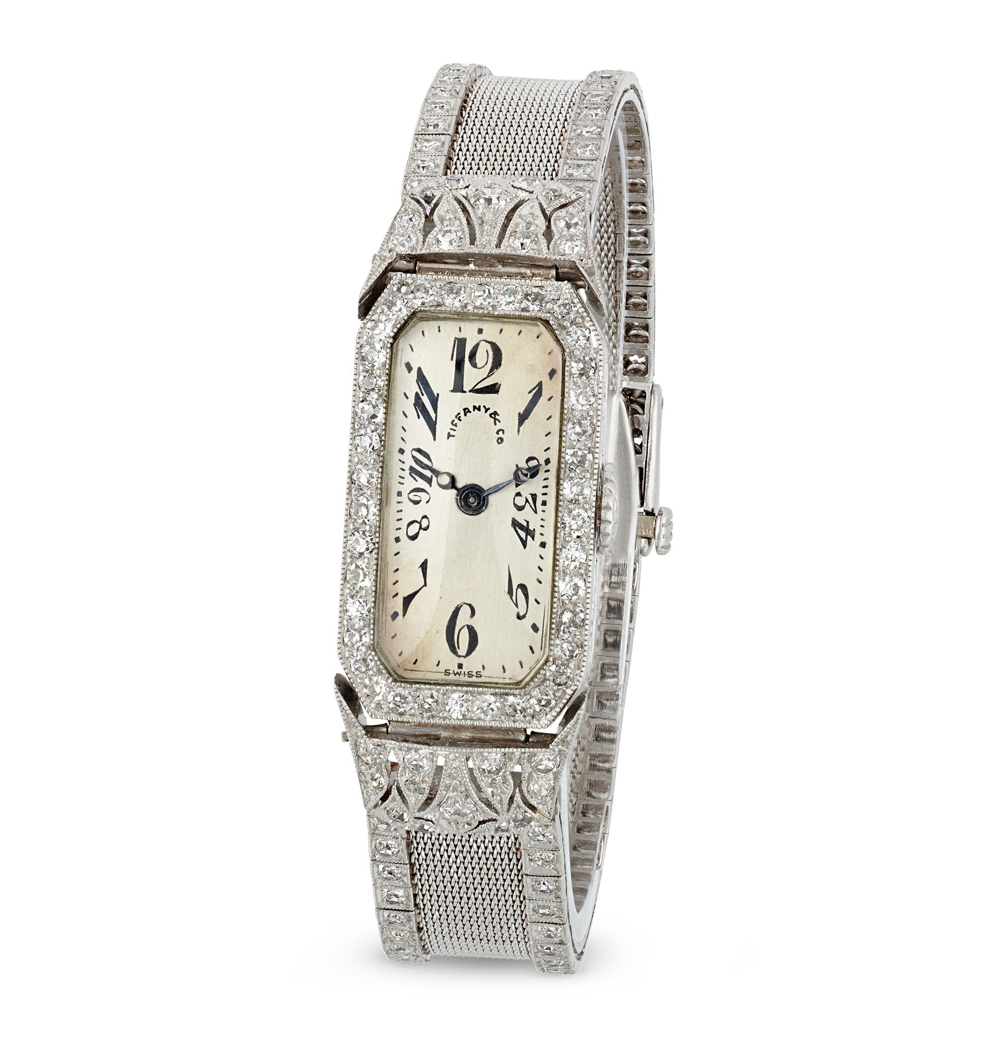 Esempio di eleganza Art Déco, questo squisito orologio da polso di Oscar Heyman per Tiffany & Co. è un capolavoro di design e artigianato. Il quadrante color crema è impreziosito da numeri arabi esplosi in stile Art Déco e lancette a pomme. La cassa