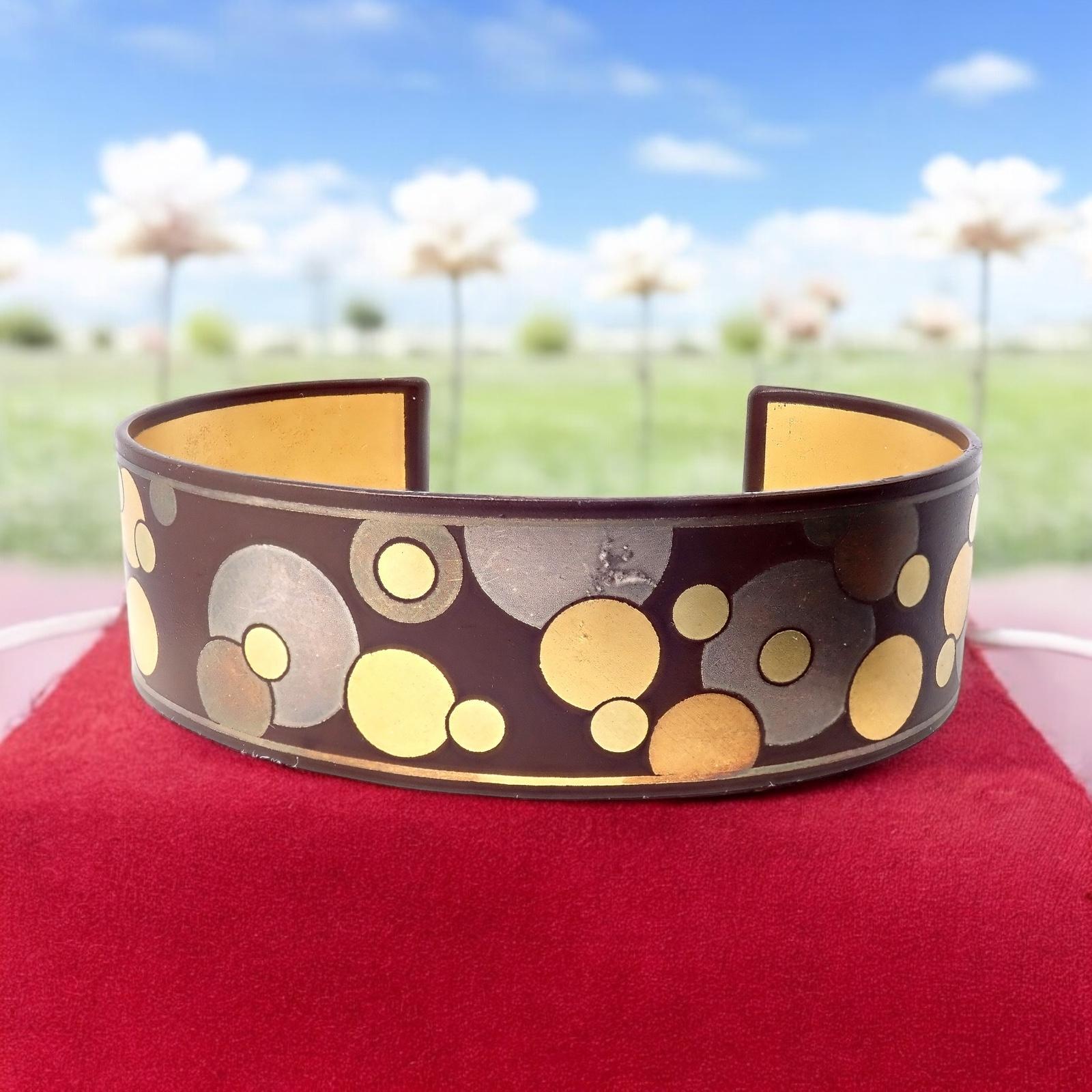 Indulge in the distinctive artistry of this Rare Vintage Tiffany & Co. Angela Cummings cuff bracelet from the 1970s. 

Forged in black iron, the cuff showcases a warm dark chocolate brown hue adorned with whimsical, overlapping 24k gold circles in