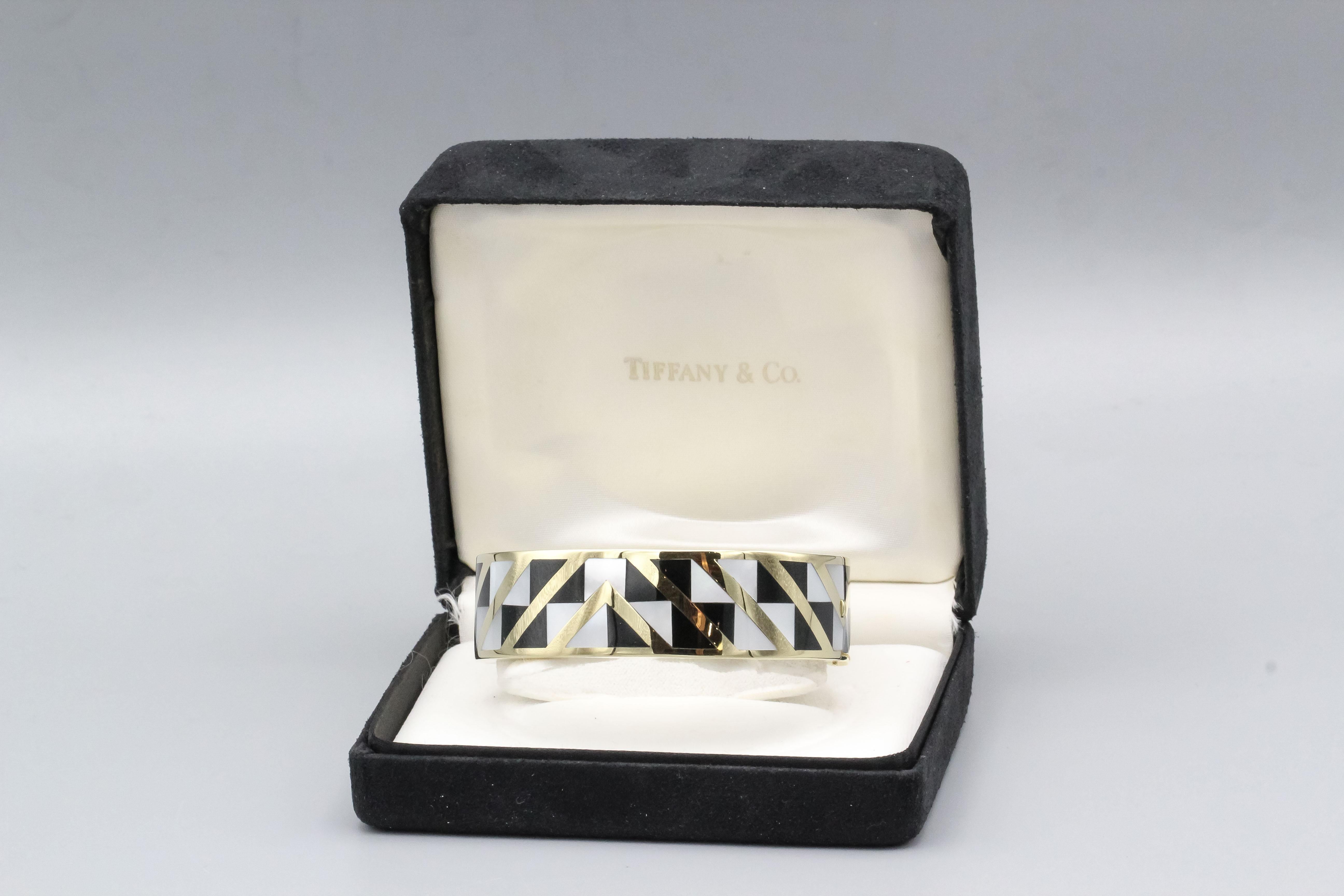 Fine 18K yellow gold bangle bracelet with inlaid mother of pearl and black jade, by Tiffany & Co. designed by Angela Cummings circa 1970s. It features a desirable geometric pattern that is stylish and distinctive.  Will comfortably fit a 6-6.5