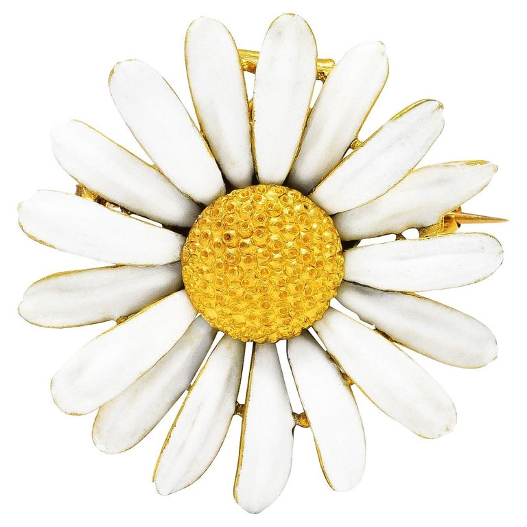 Designed as a highly rendered daisy with texturous center and fanning petals. Grooved with opaque matte white enamel - exhibiting minimal loss. Reverse is decorated with rendered gold foliate. Completed by hinged pin stem. With locking closure and