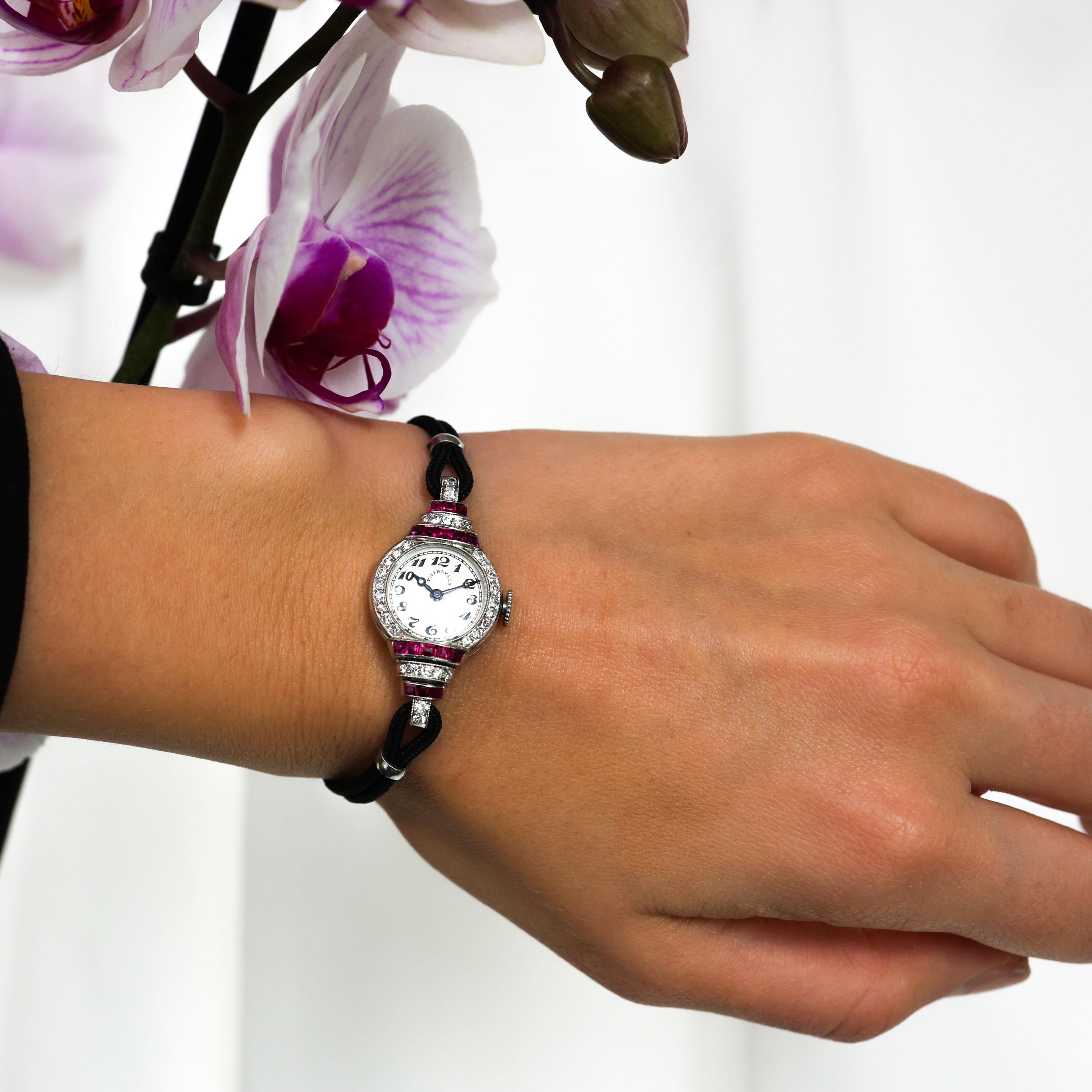 Un reloj de pulsera Tiffany & Co., Art Déco, de rubíes, diamantes y platino, con esfera circular blanca, con números árabes negros, firmado Tiffany & Co., con agujas de acero azul, con corona de cuerda, con cristal curvado, rodeado de diamantes