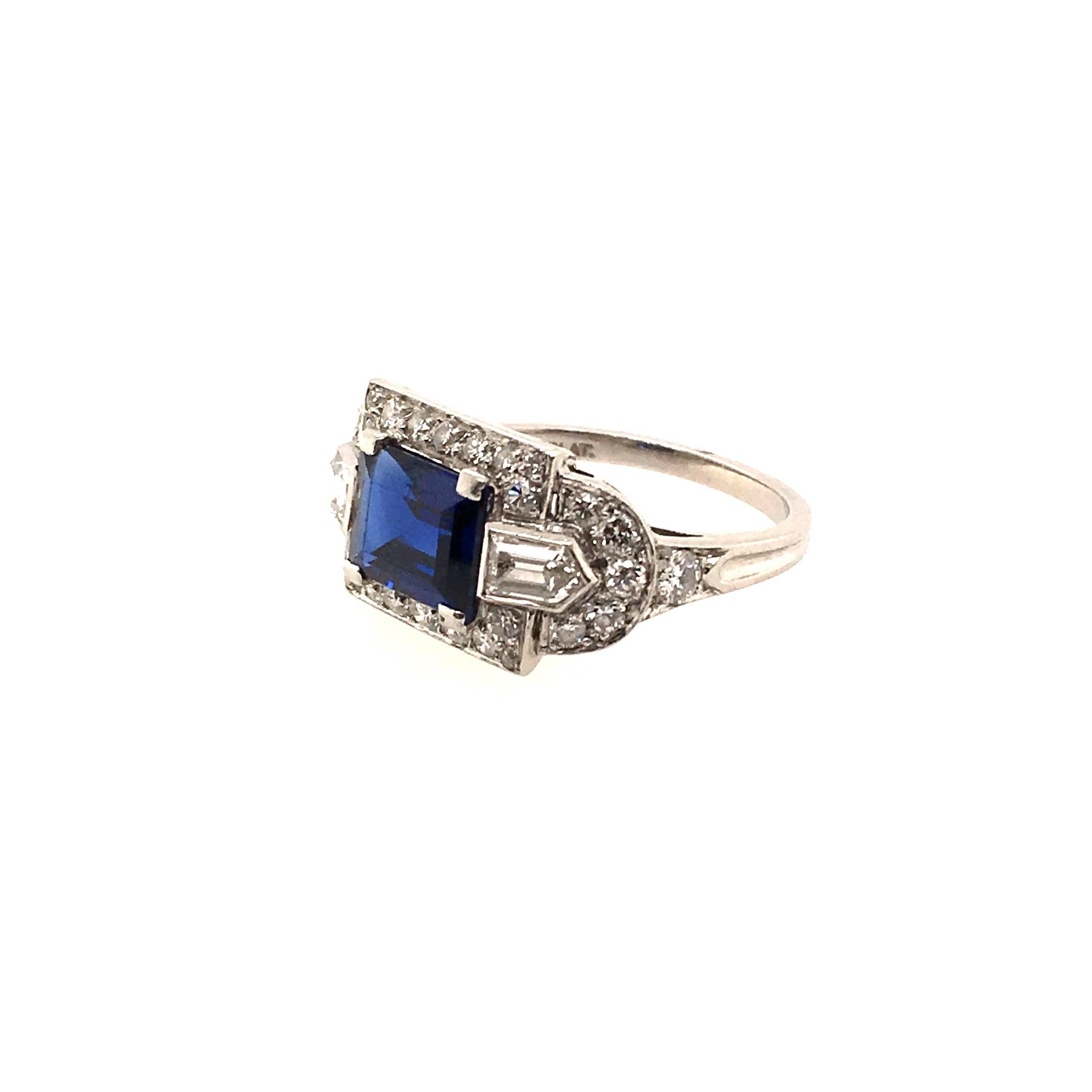 A late Art Deco platinum, sapphire and diamond ring. Tiffany & Co.  Designed as a pave set diamond rectangular plaque, centering a horizontally set  emerald cut sapphire, weighing approximately 1.80 carats, enhanced by bullet cut diamond shoulders.