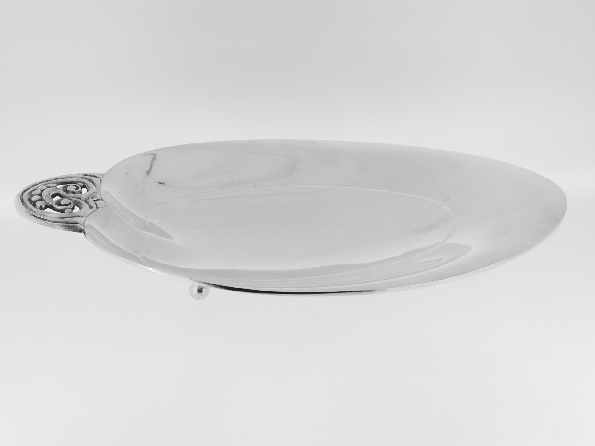 A fine Art Deco oval, footed bowl.

By Tiffany & Co. 

In sterling silver.

With a large, slightly lobed oval or heart shaped bowl fixed with an open work tab handle and supported on four ball feet 

Fully hallmarked to the base, including an M