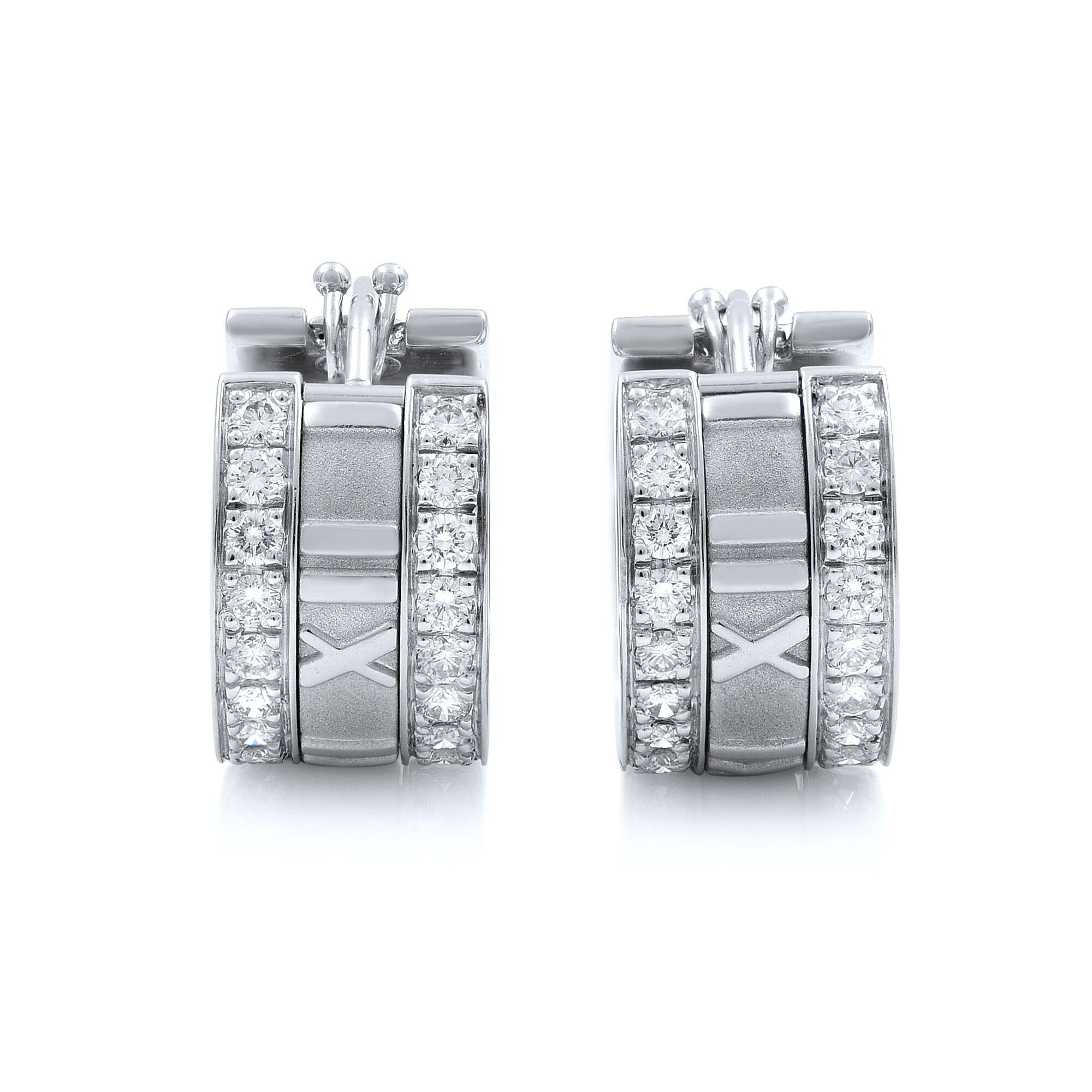 Tiffany & Co white gold diamond earrings from Atlas collection. They are crafted in solid 18kt white gold with polished and textured finish. Small wide band huggie design and a round cut sparkling diamond adorned on the front edge of the earrings