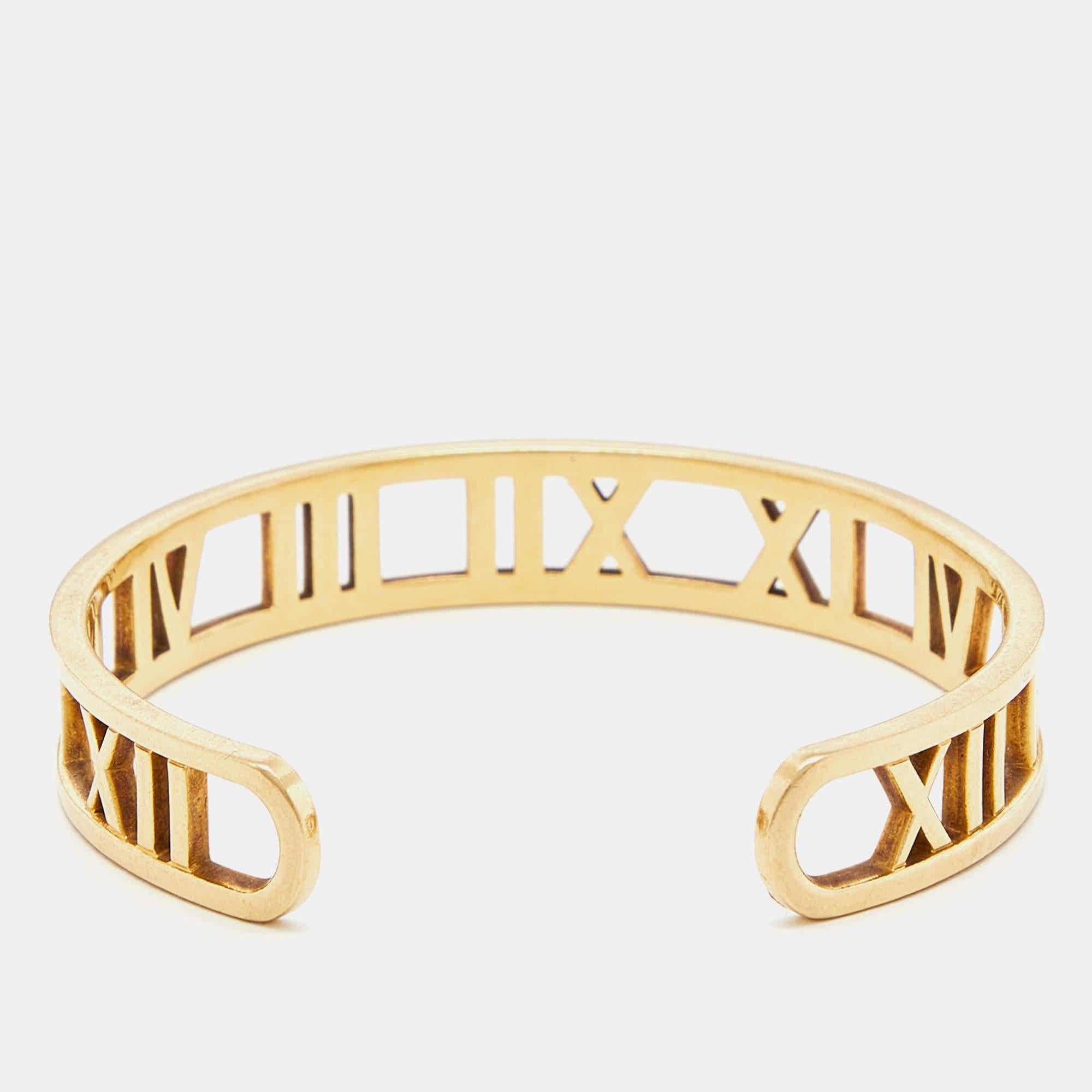 This 28k yellow gold open cuff bracelet from Tiffany & Co. is from their Atlas line. The cuff is sleek and sophisticated in its design. A linear arrangement of Roman numeral motifs is debossed across the bracelet to bring forth the allure of the