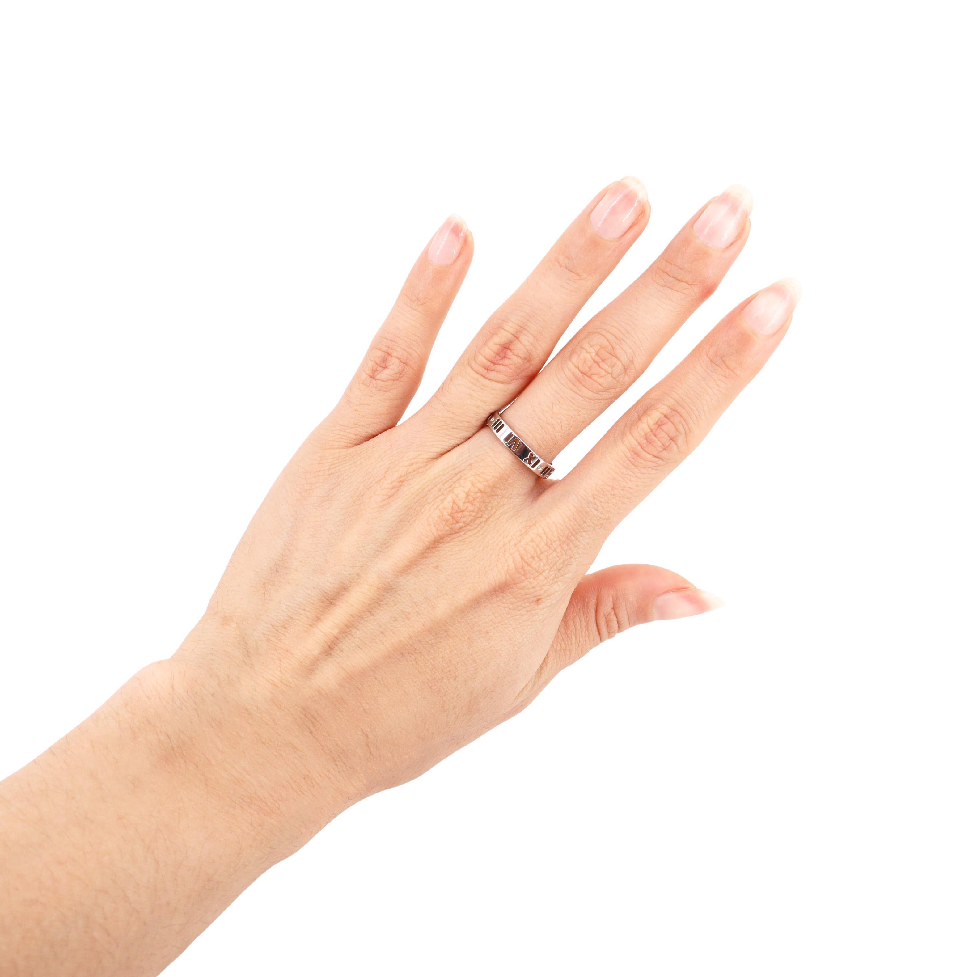Presenting the Tiffany & Co. Atlas bandRing, meticulously crafted from 18K white gold, elegantly engraved with Roman numerals. This exquisite ring features four round-cut diamonds, with a total weight of approximately 0.04 carats, showcasing F