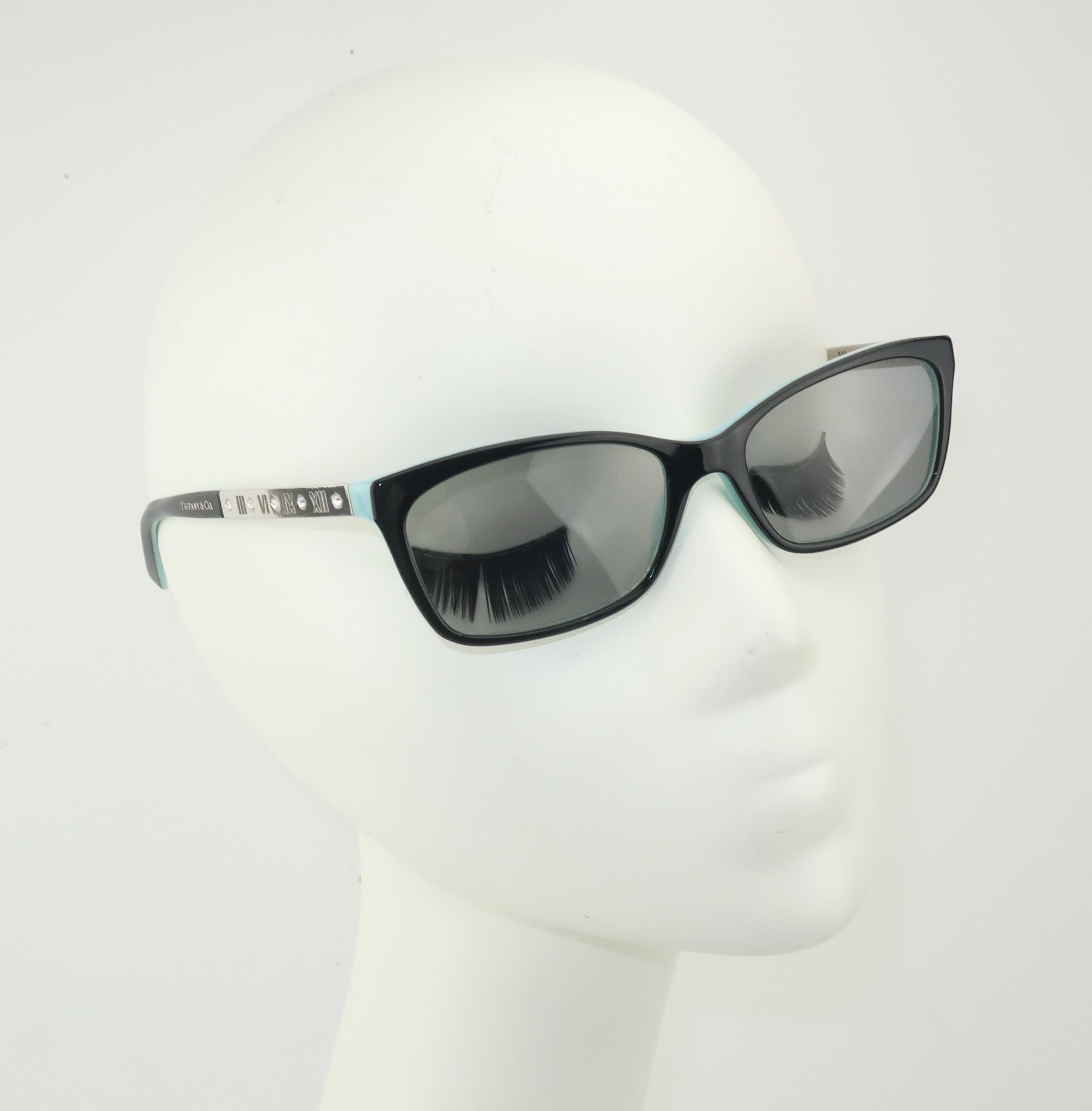 The Italian luxury eyewear brand, Luxotica, creates a classic rectangular frame for Tiffany & Company.  The black frame is lined in Tiffany's signature blue and features silver arms accented by Roman numerals and sparkling crystals.  The gray lenses