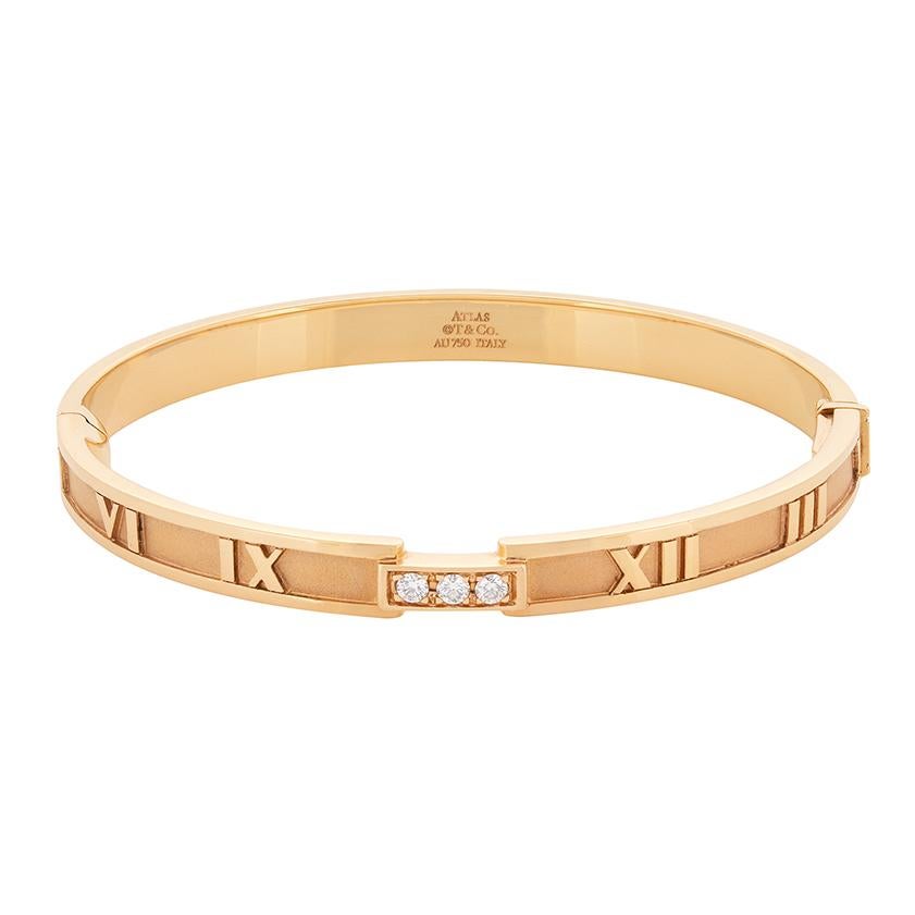 Ce magnifique bracelet fait partie de la collection 'Atlas' de Tiffany & Co. Réalisée en or rose 18 carats, cette pièce présente des chiffres romains sur le pourtour du bracelet et est ornée de trois diamants d'un poids total de 0,15 carat, sertis
