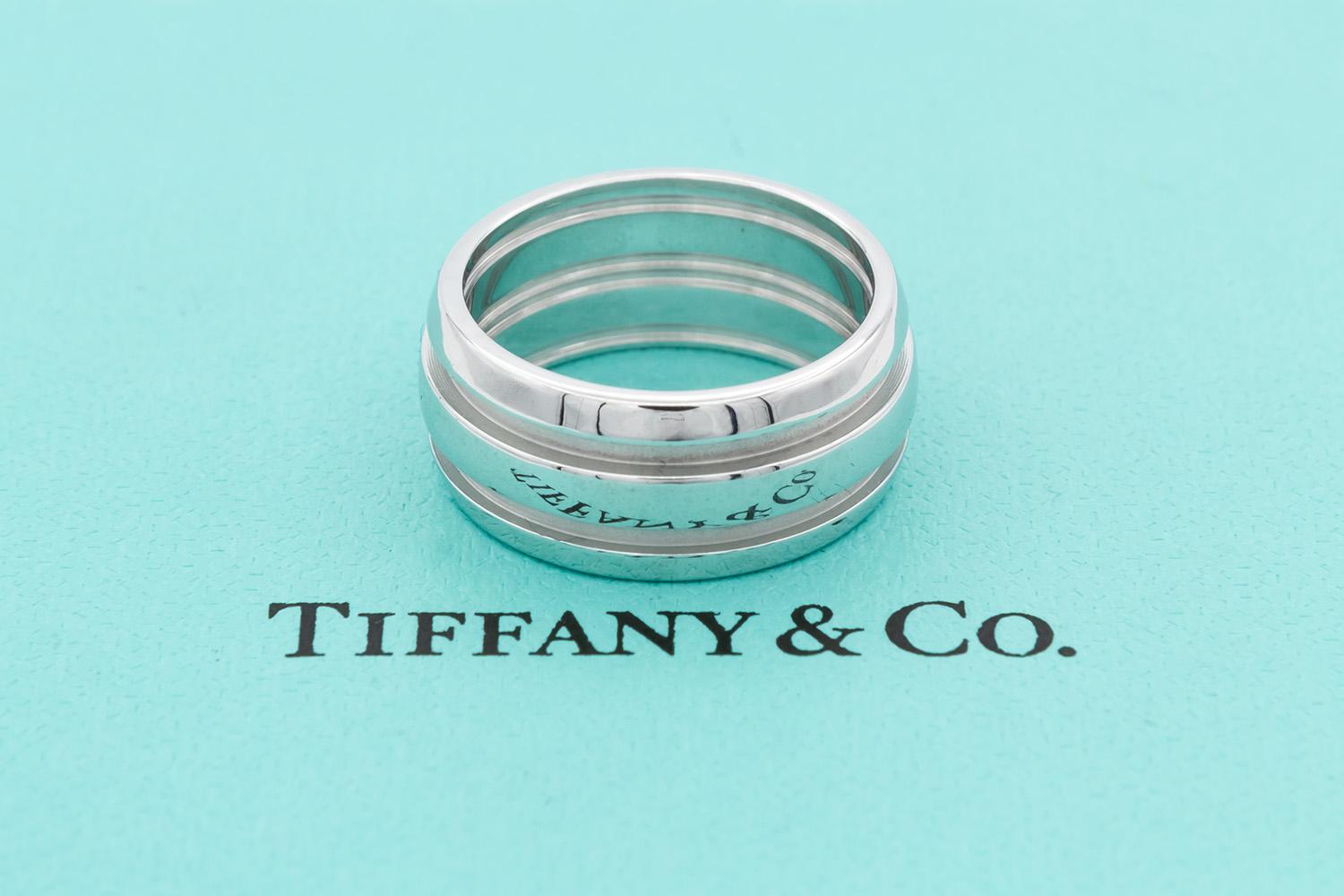 We are pleased to offer this Authentic Tiffany & Co. Atlas Double Groove 18k White Gold Band Ring. It features the classic Atlas styling with a double groove. It is a size 7 US and measures 9mm wide. It comes with the Tiffany ring box. The ring is