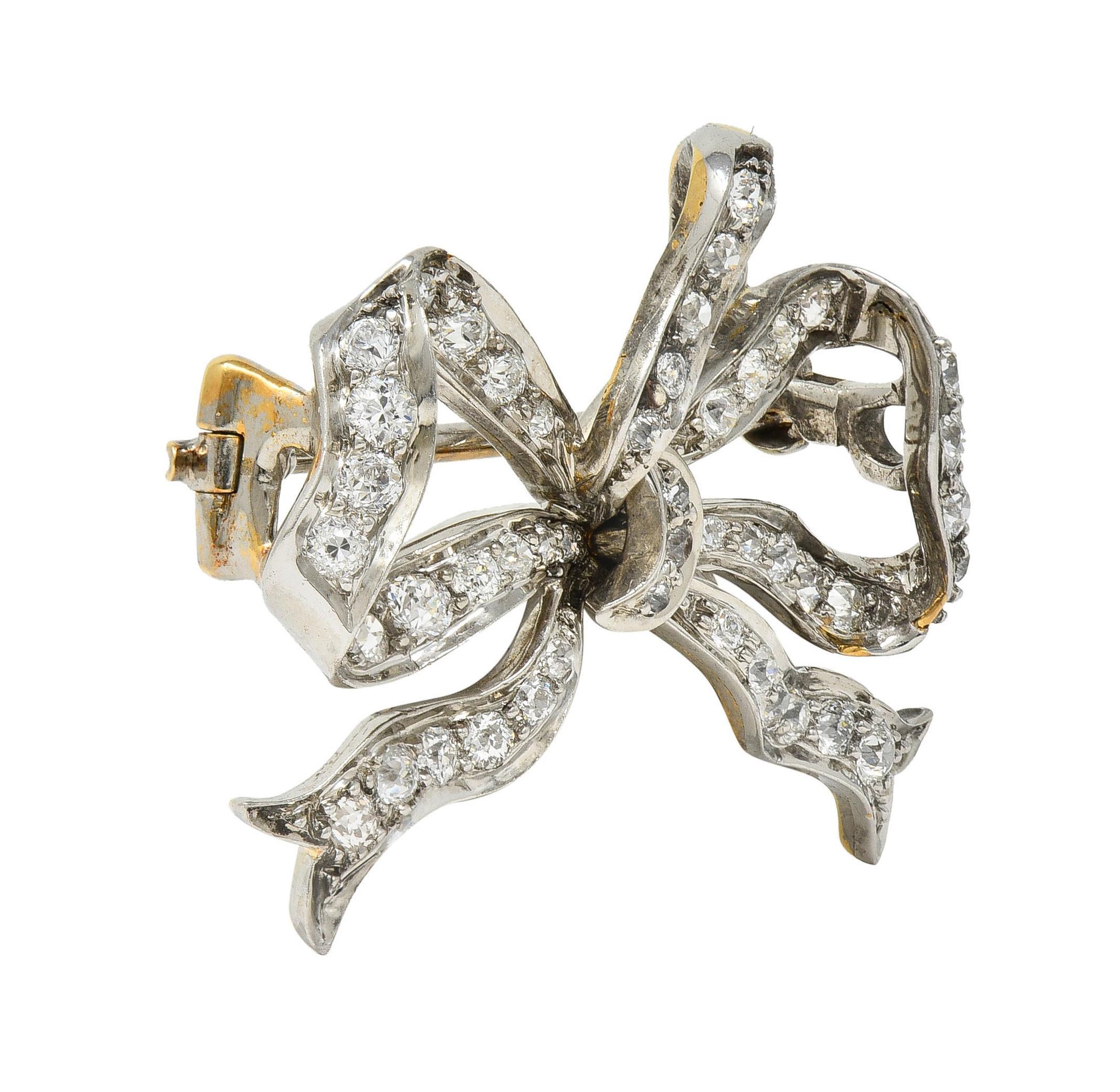 Designed as a dimensional bow of tied ribbon comprised of platinum-topped gold
Bead set throughout with old European cut diamonds
Weighing approximately 1.12 carats total 
G/H color with VS2 to SI1 clarity
Completed by hinged pinstem with locking