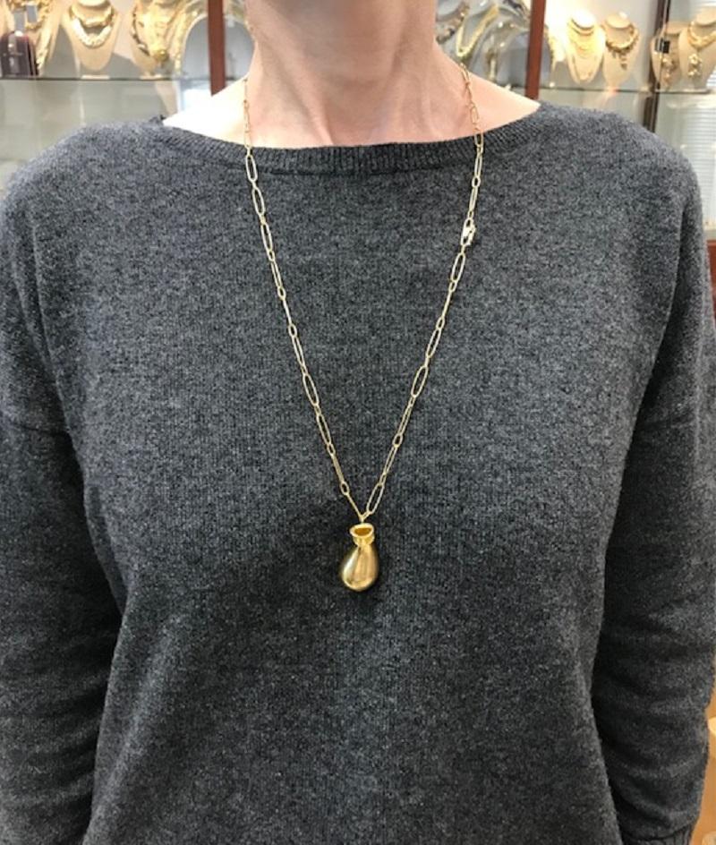 This Elsa Peretti necklace for Tiffany & Co. features her iconic Jug pendant design, crafted in 18k gold. The pendant has a soft, organic shape reminiscent of a small vessel or amphora, with smooth curves that give it a fluid quality. It's suspended