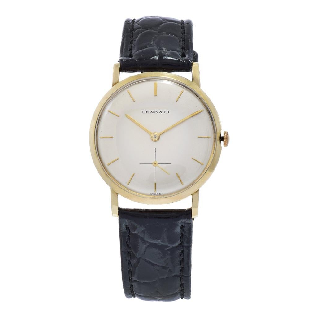 Die zeitlose Tiffany 1950's 14KT Gold Watch mit einem runden 32mm Gehäuse ist ein wahres Symbol für raffinierten Luxus. Dieser exquisite Zeitmesser verfügt über ein raffiniertes beigefarbenes Zifferblatt mit vollgoldenen Strichindizes, das Eleganz