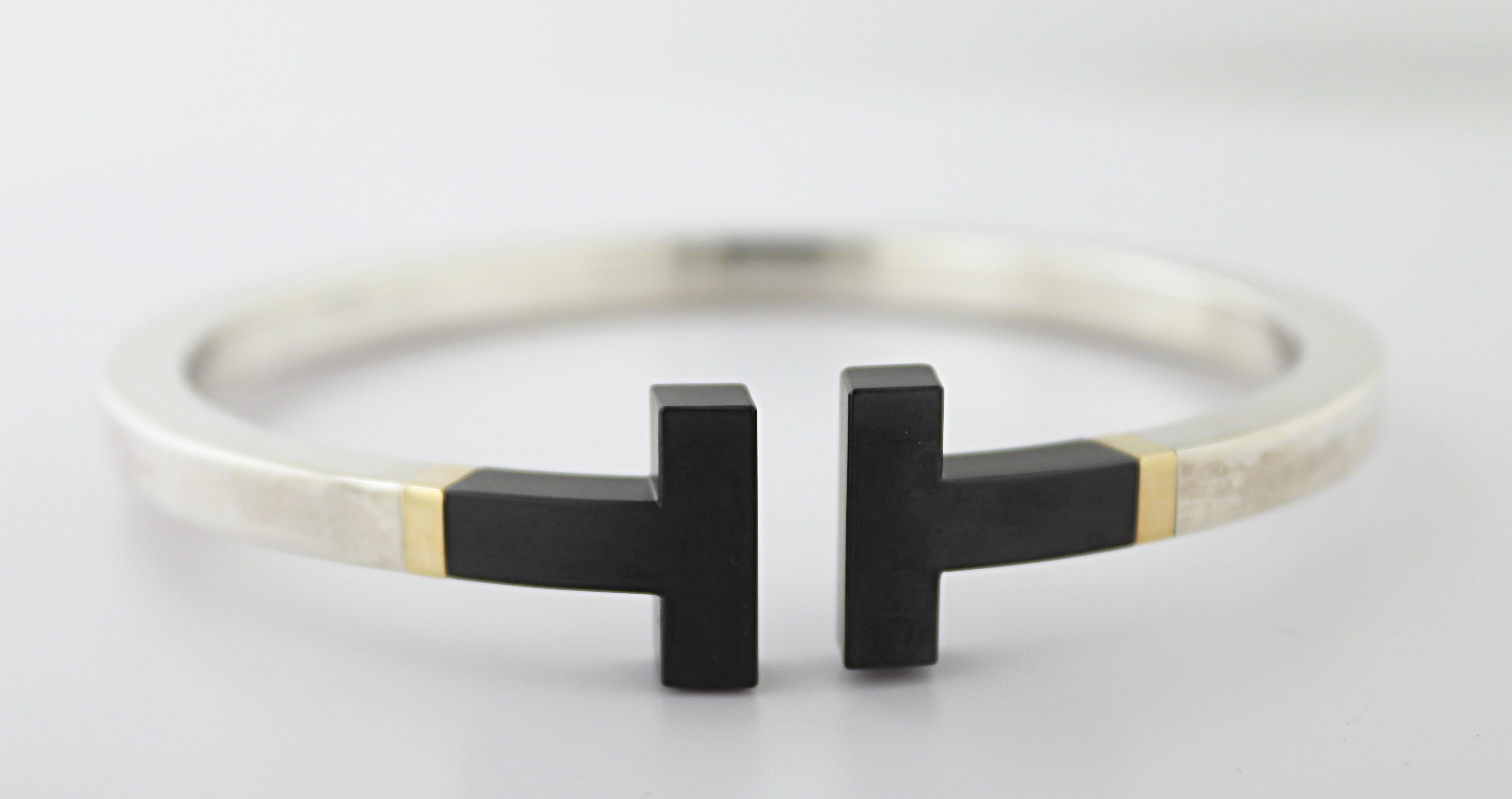 Designed with (2) squared black ceramic “T”’s, set in a squared sterling silver hinged bangle, 14.90 X 4.8
X 4.8 mm, internal diameter 65.1 mm, marked © TIFFANY & CO. AG925 GERMANY, AU750, Gross weight
27.50 grams.