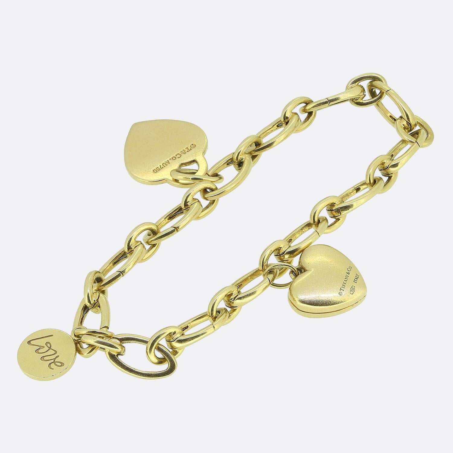 Nous avons ici un bracelet à breloques emblématique du célèbre créateur de bijoux Tiffany & Co. Réalisé en or jaune 18ct, ce bracelet est formé d'une série de maillons ovales à la finition lisse. Le bracelet est ensuite accompagné d'un trio de