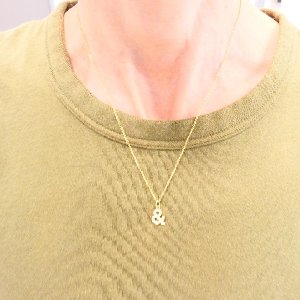 Este collar de diamantes Tiffany & Co. incluye un delicado dije de ampersand, engastado con pavé de diamantes en oro amarillo de 18k. 
El colgante tiene la forma del icónico símbolo 