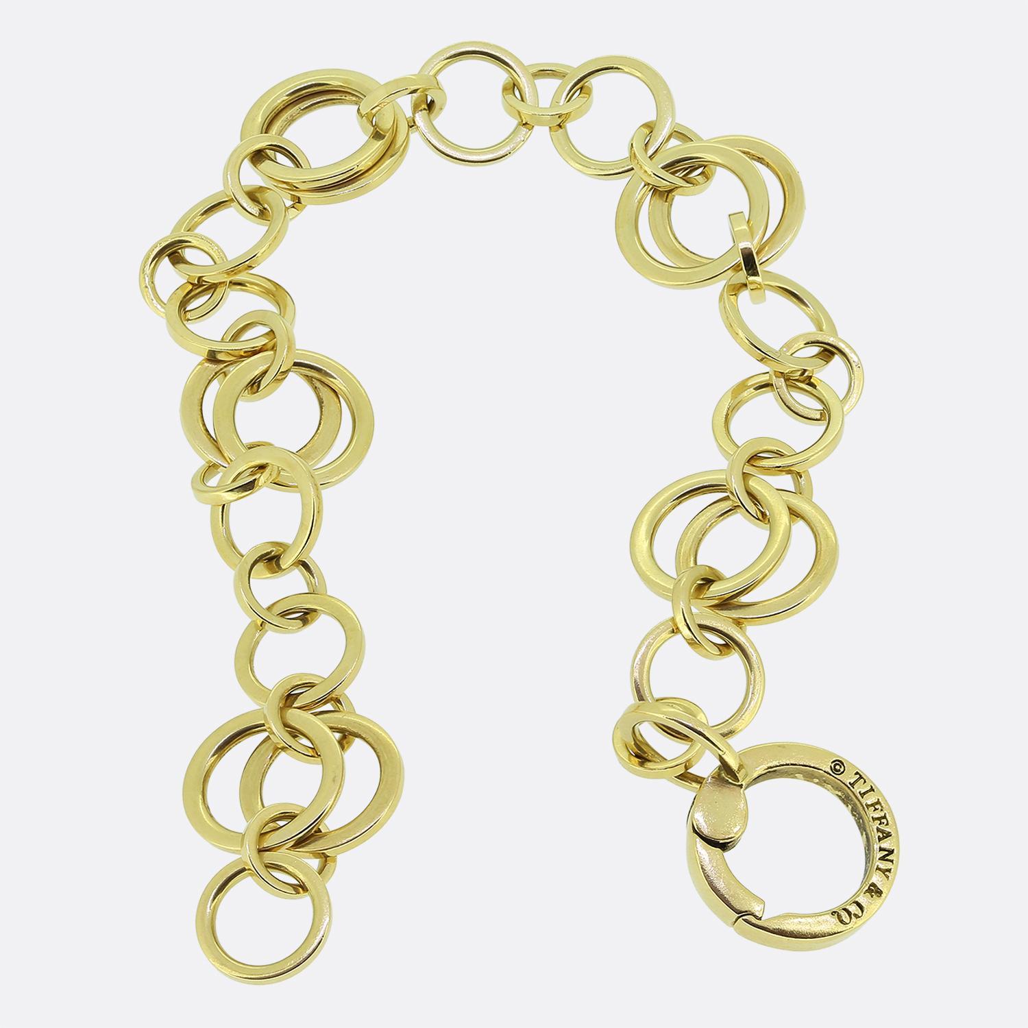 Aquí tenemos una distinguida pulsera del mundialmente conocido diseñador de joyas Tiffany & Co. Esta pieza presenta una serie de eslabones circulares entrelazados de distintos tamaños elaborados en cálido oro amarillo de 18 ct para crear un