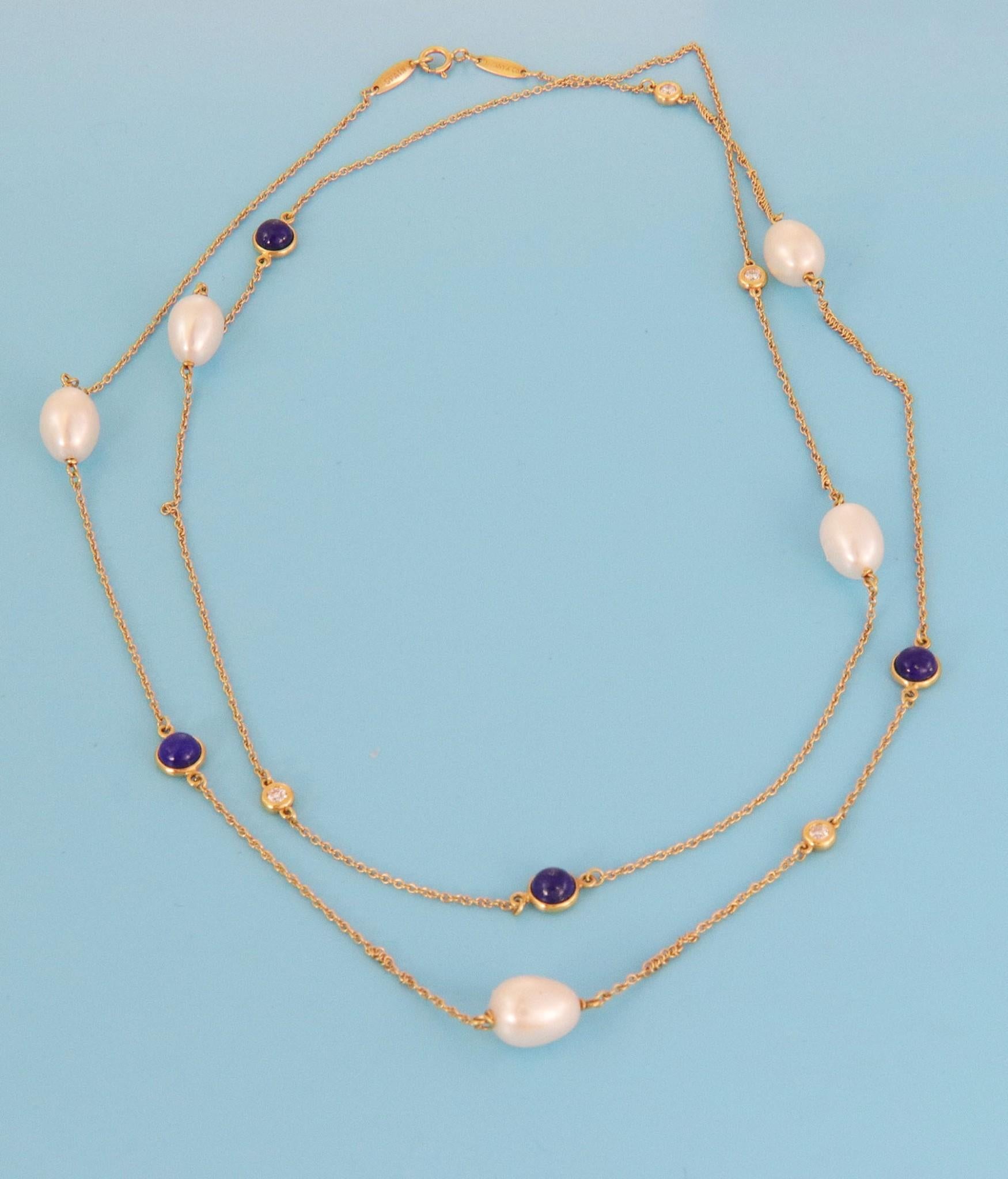 Fabulous and authentic from Tiffany & Co. by designer Elsa Peretti from her Color By The Yard Collection. This long necklace is crafted from 18k yellow gold featuring 5 oval shape shimmering pearls attached to the chain with 4 round bezel set lapis