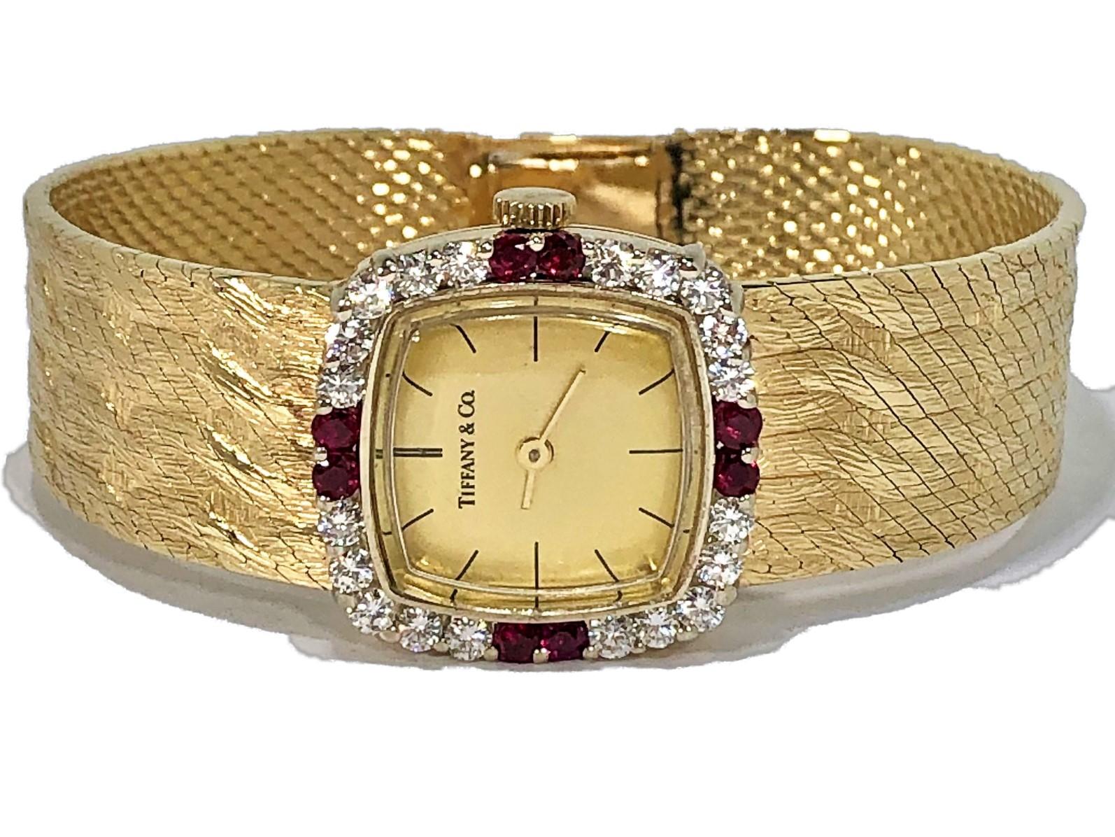 This elegant champagne dial 14K Yellow Gold Tiffany 
& Co. wristwatch with a cushion shaped diamond bezel,
is set with 2 brilliant rubies at the 12 o'clock, 3 o'clock, 
6 o'clock, and 9 o'clock positions .The head measures
7/8 inch wide (not