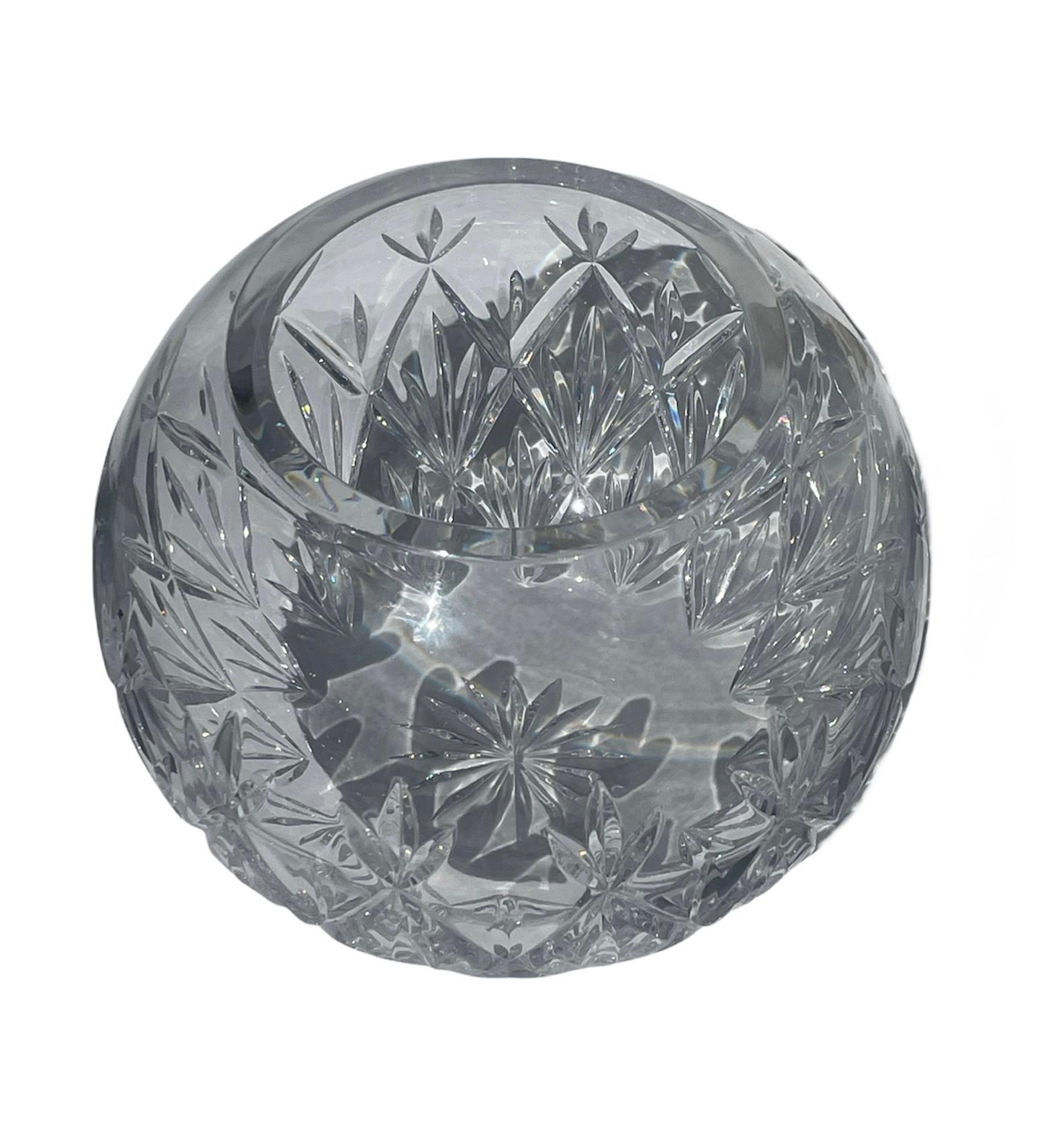 This is a Tiffany & Co. cut clear crystal round bowl vase. It depicts multiple diamonds and kind of Fleur de lis patterns around it. In the crystal surface of the center of the base, there is a starburst. Below the vase, it is the acid etched
