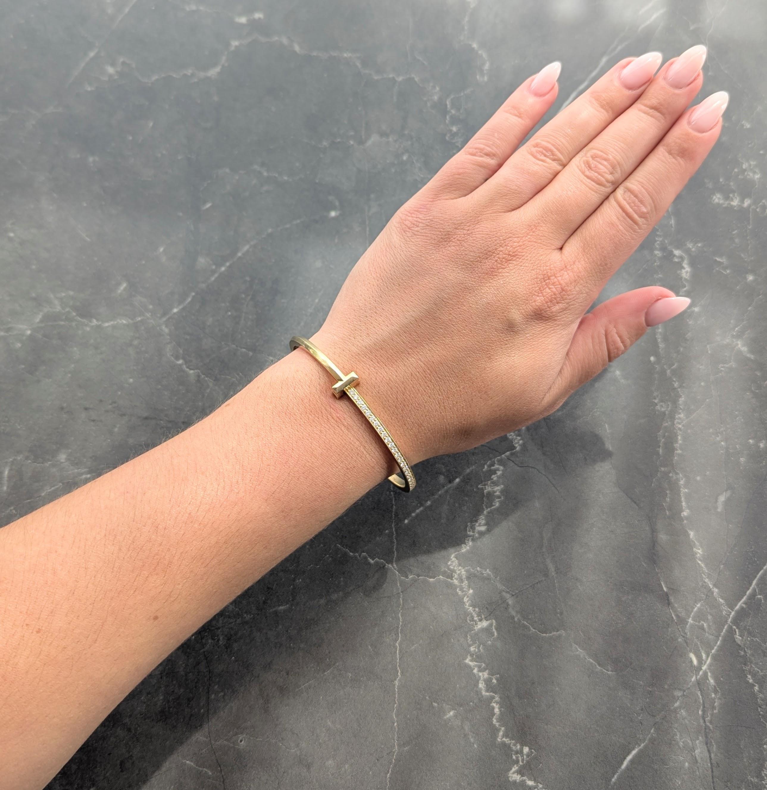 Designed as a hinged yellow gold bangle bracelet centering a faceted 'T' motif
One half is faceted high polish gold and the other is bead set with diamonds
Round brilliant cut and weighing 1.07 carats total - E-F color with VS clarity
Opens on a