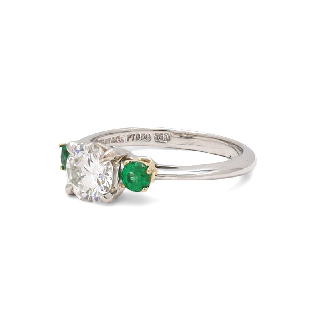 Authentic Tiffany & Co. ring crafted in platinum and set with a stunning 0.71 carat GIA certified Diamond (I/VVS1) and two lively emeralds with a deeply saturated yellowish-green hue, weighing approximately 0.10 carat each. US size 4 3/4. Signed