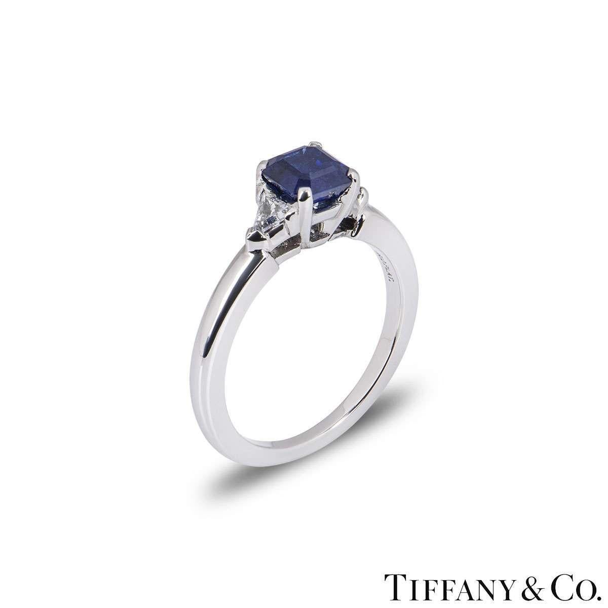 A platinum diamond and sapphire ring by Tiffany & Co. The ring is set to the centre with a step cut blue sapphire weighing approximately 0.50ct. The sapphire is complemented by two trilliant cut diamonds totalling approximately 0.30ct. The ring is