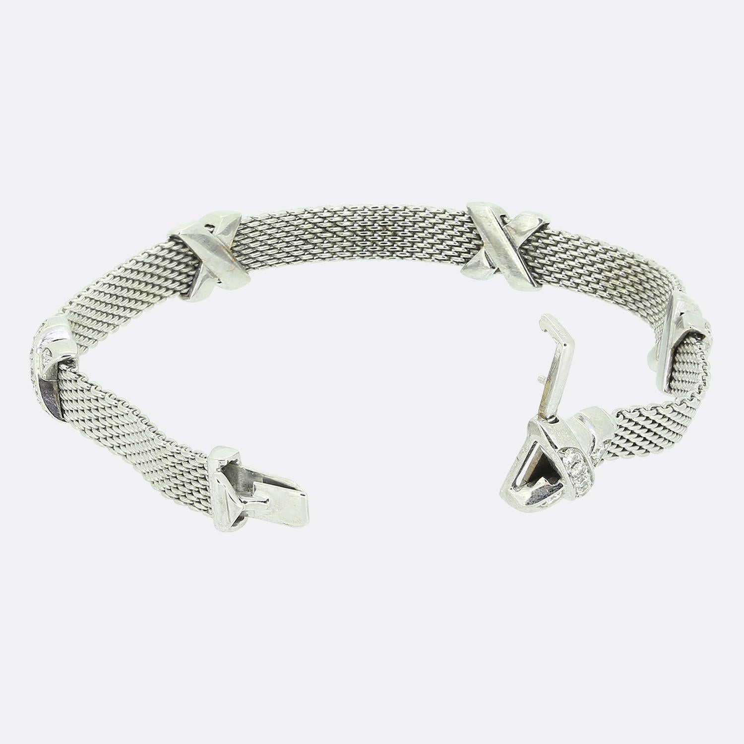 Aquí tenemos una pulsera de diamantes de oro blanco de 18 ct del mundialmente conocido diseñador de joyas de lujo Tiffany & Co. La pulsera se compone de una banda estilo malla con cinco motivos de cruces de diamantes. Cada cruz está engastada con