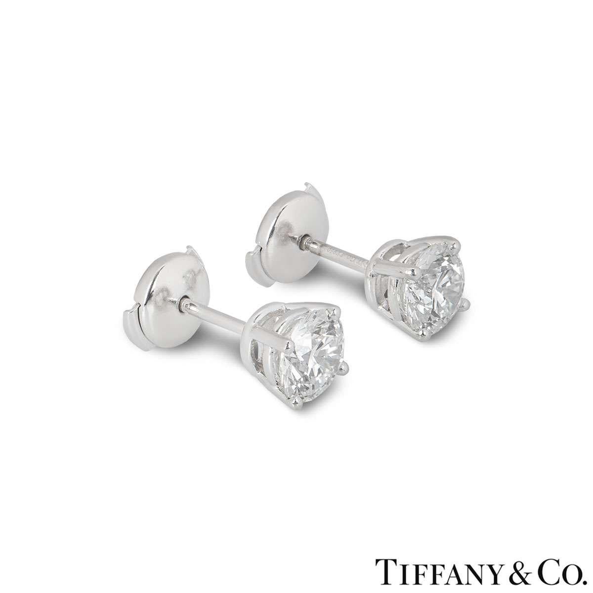 A pair of diamond stud earrings by Tiffany & Co. The earrings each feature a single round brilliant cut diamond in a 4 claw setting weighing 1.21ct and 1.22ct. The diamonds are both G colour and VS1 clarity. The earrings have post and alpha back