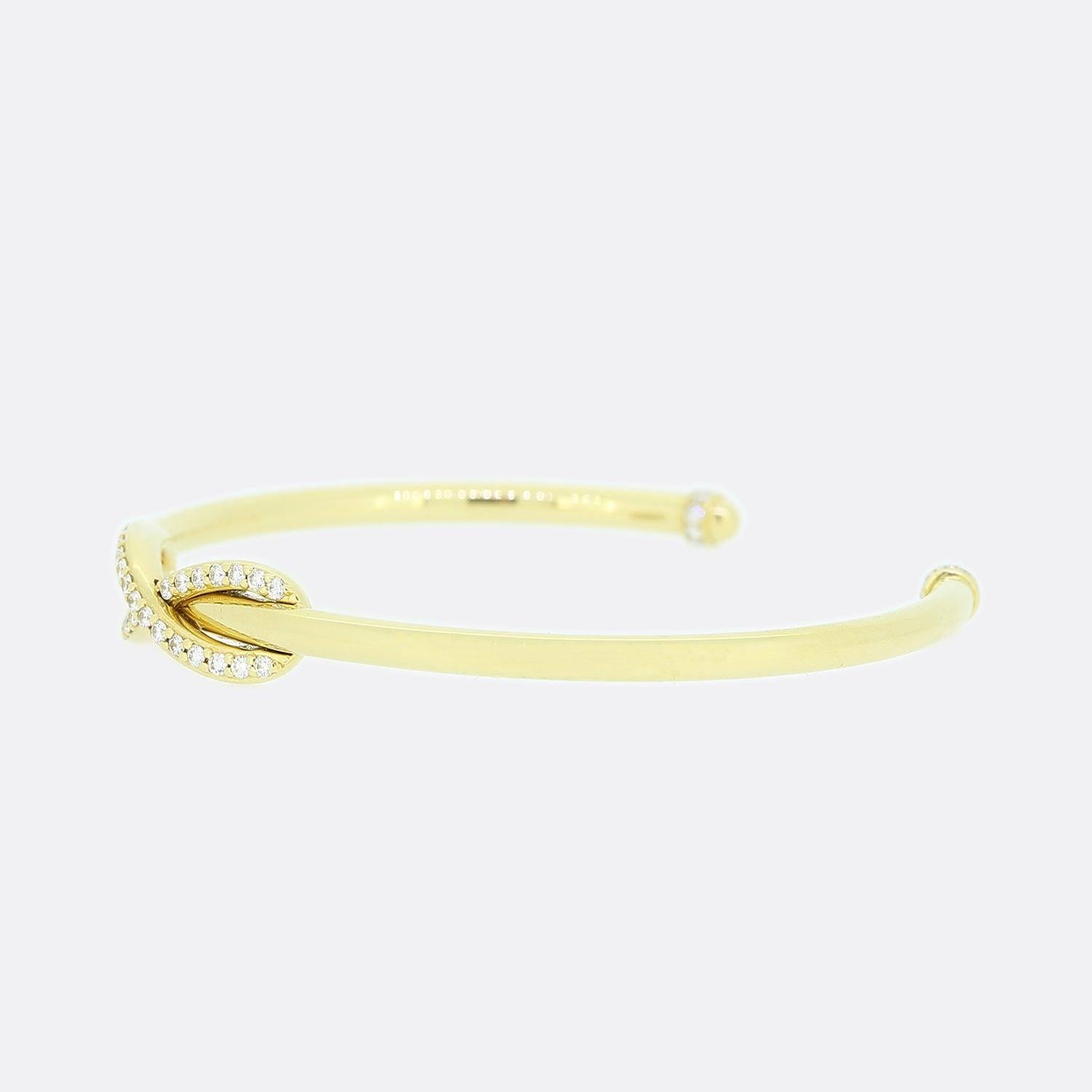This is an 18ct yellow gold diamond bangle from the luxury jewellery designer Tiffany & Co. The bangle features a central diamond set infinity symbol with a plain polished finish. Each point at the end of the cuff has also been set with eight round