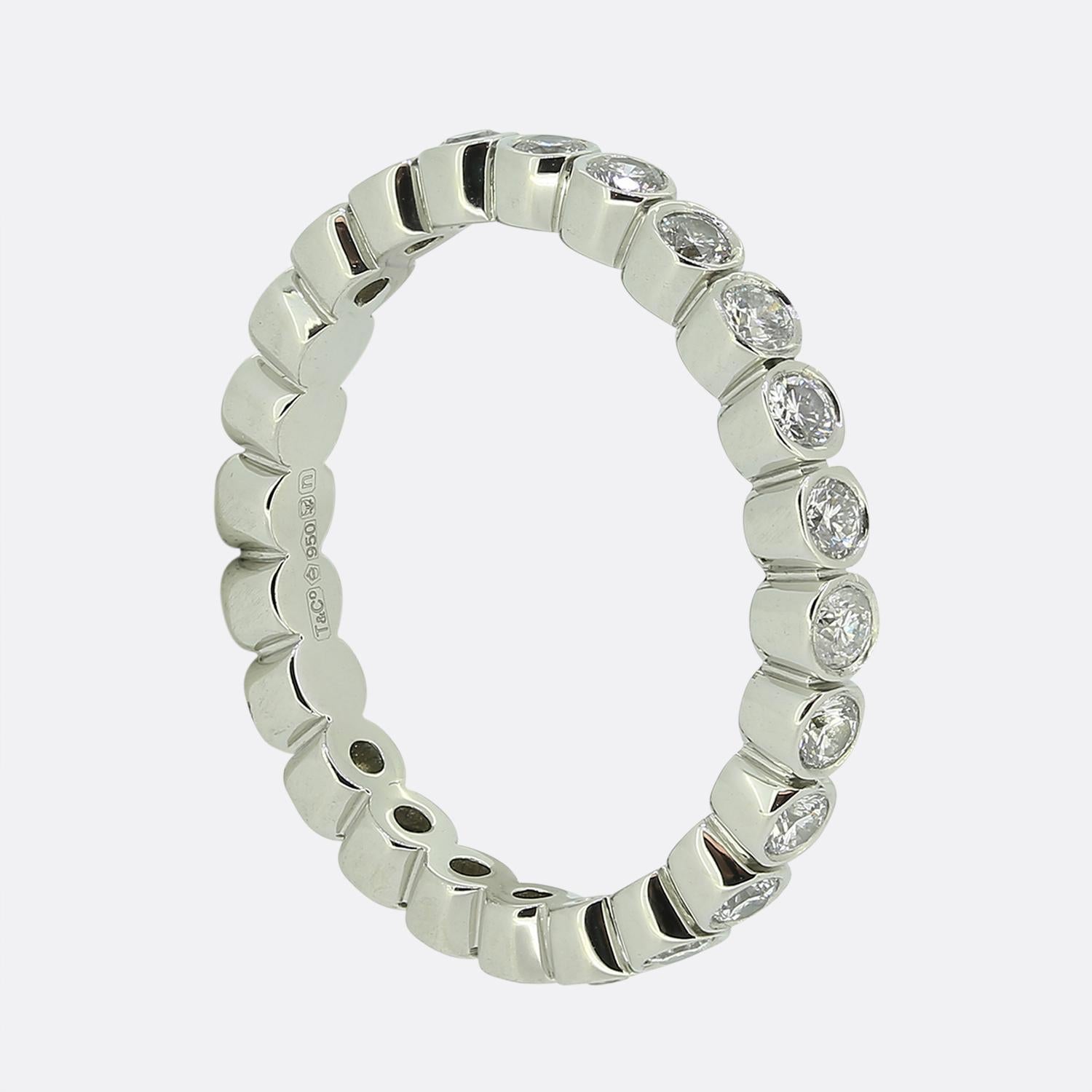 Here we have a sophisticated diamond eternity band from the world renowned jewellery designer, Tiffany & Co. This exquisite piece features a single line of bright round brilliant cut diamonds, each securely set in a bezel setting, encircling the
