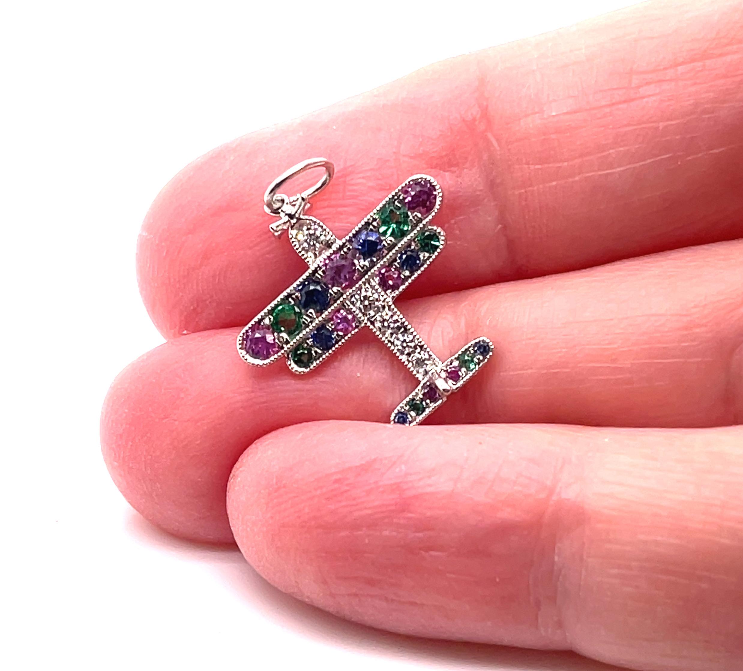 This is an adorable authentic plane charm or pendant from Tiffany & Co. It is crafted from platinum featuring a double wing set with pink and blue sapphires and has green tsavorite with diamonds, all bordered around the edge with fine milgrain