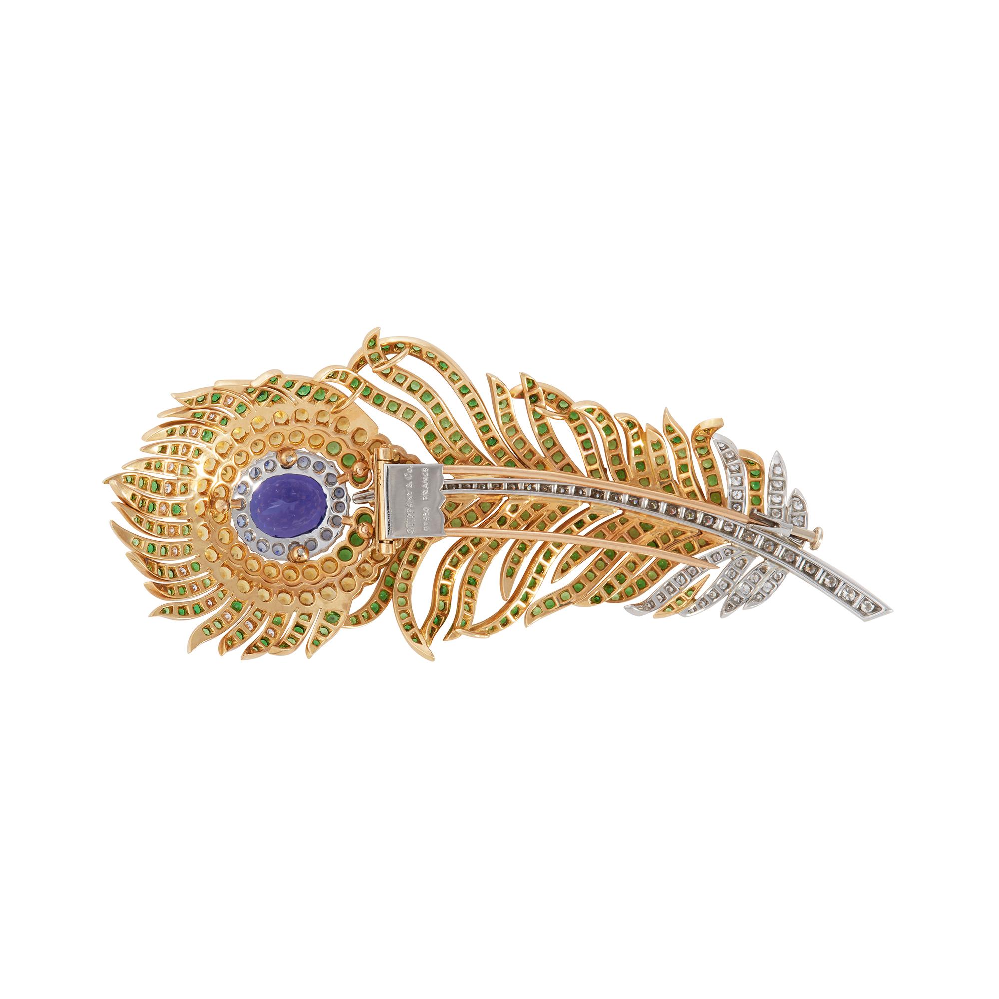 Authentic Tiffany & Co. brooch crafted in 18 karat yellow gold and platinum to resemble a peacock feather. The brooch centers on an oval cut tanzanite and it is set throughout with yellow and blue sapphires, tsavorite garnets, and is accented by 82