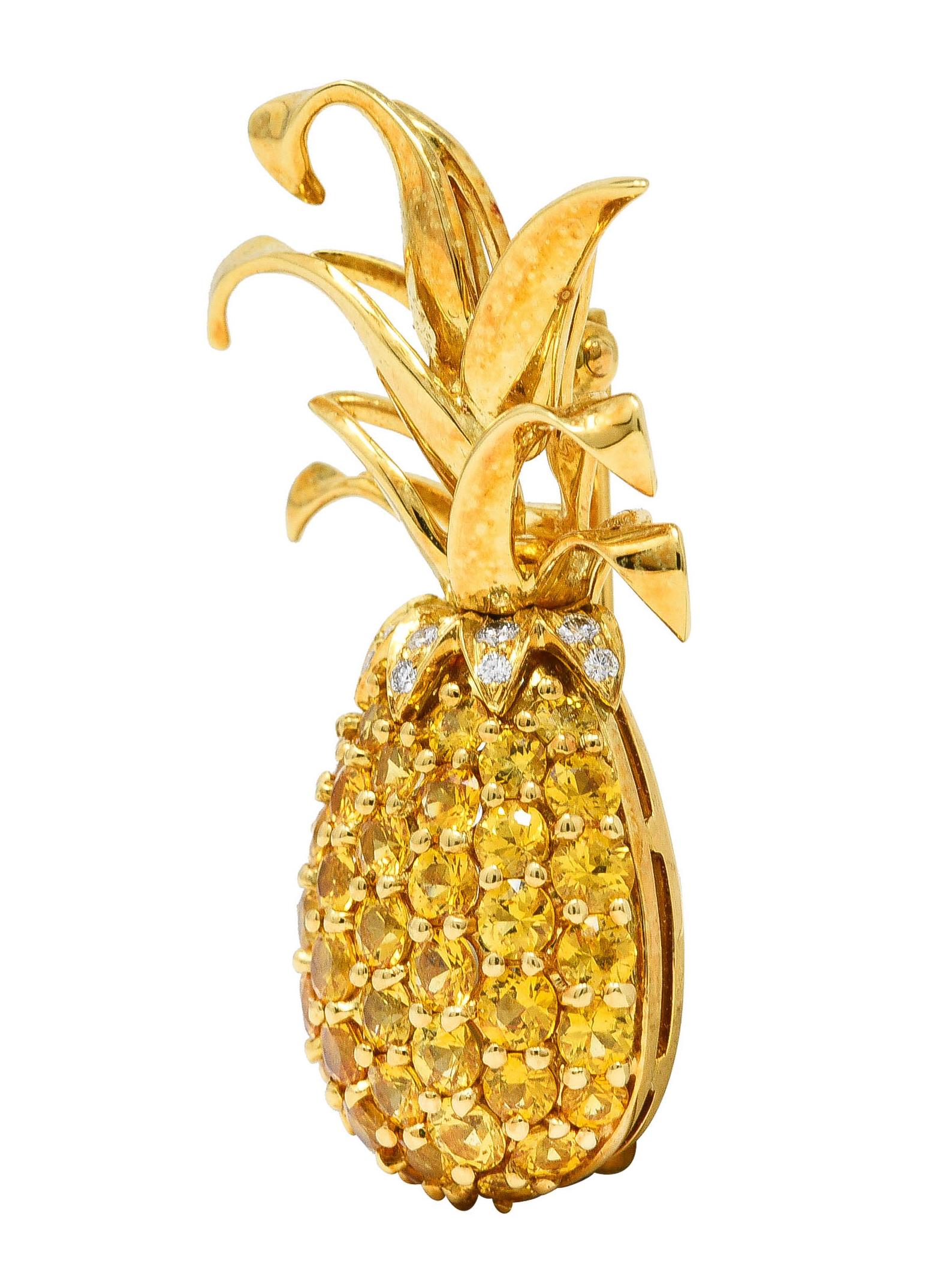 Designed as a stylized pineapple fruit with a furling crown of high polished gold leaves. Body features pavé set round cut sapphires weighing approximately 4.50 carats total. Transparent bright orangey-yellow in color with medium saturation.