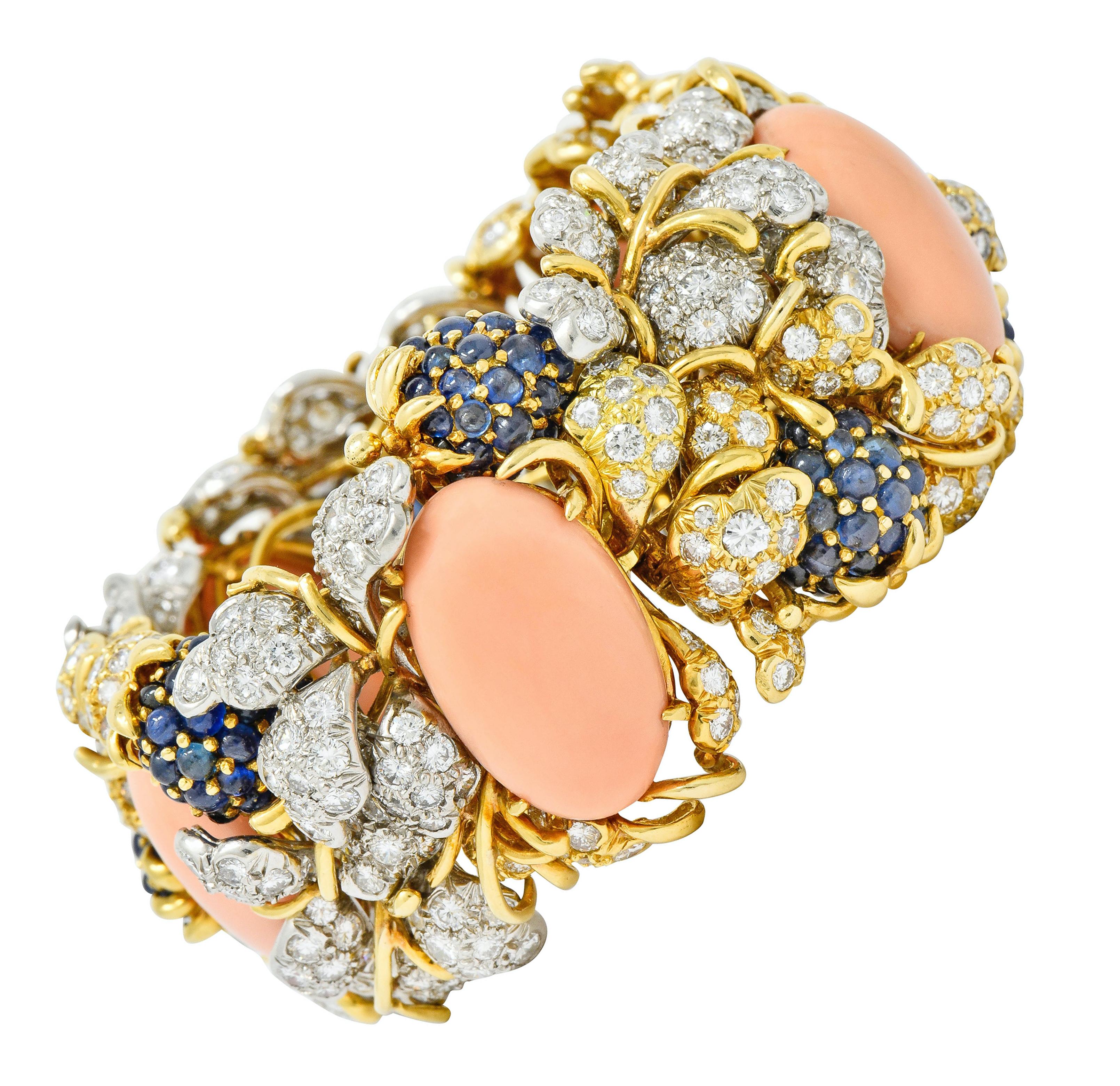 Wide bracelet designed as winding gold vines and gemmed ivy leaves with berry stations that form hidden segmentation that articulate slightly on a hinge

With five pastel orangey-pink coral cabochon prong set throughout and very well-matched,