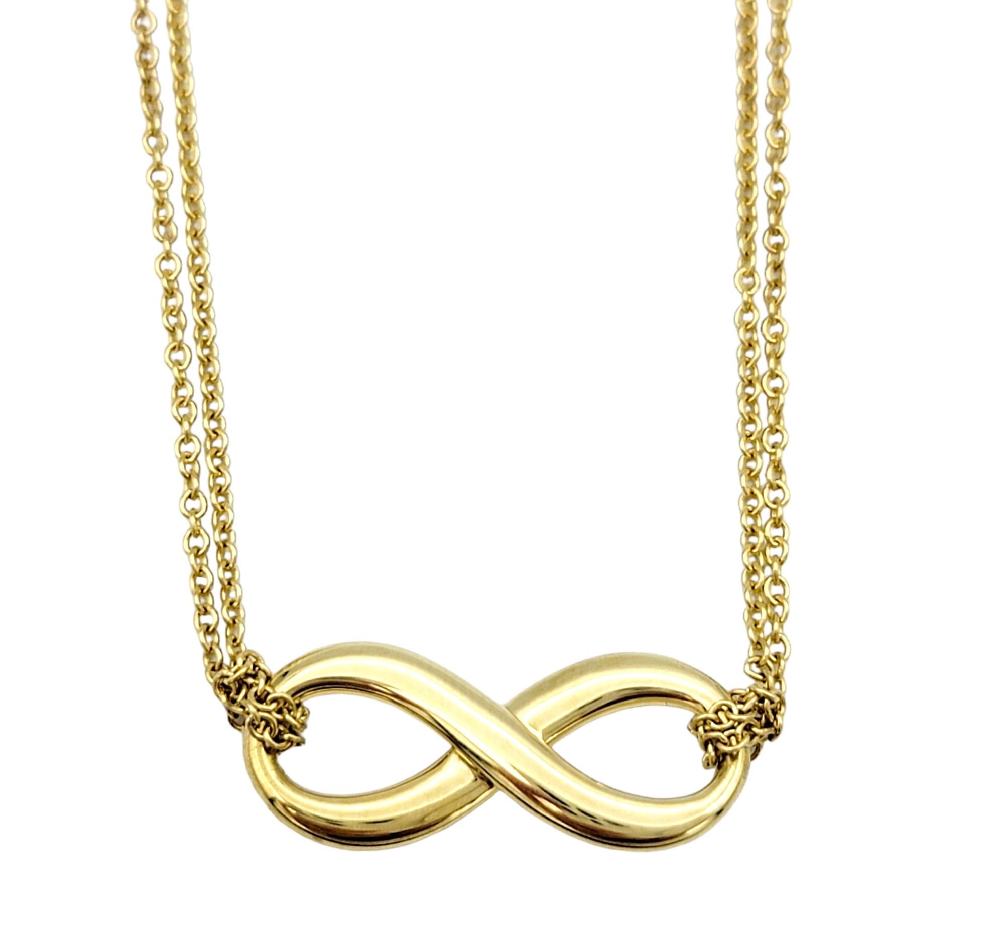 This stunning Tiffany & Co. double chain infinity pendant necklace in 18 karat yellow gold is a stunning piece of jewelry that exudes elegance and sophistication. The pendant features the iconic infinity symbol, representing eternity and everlasting