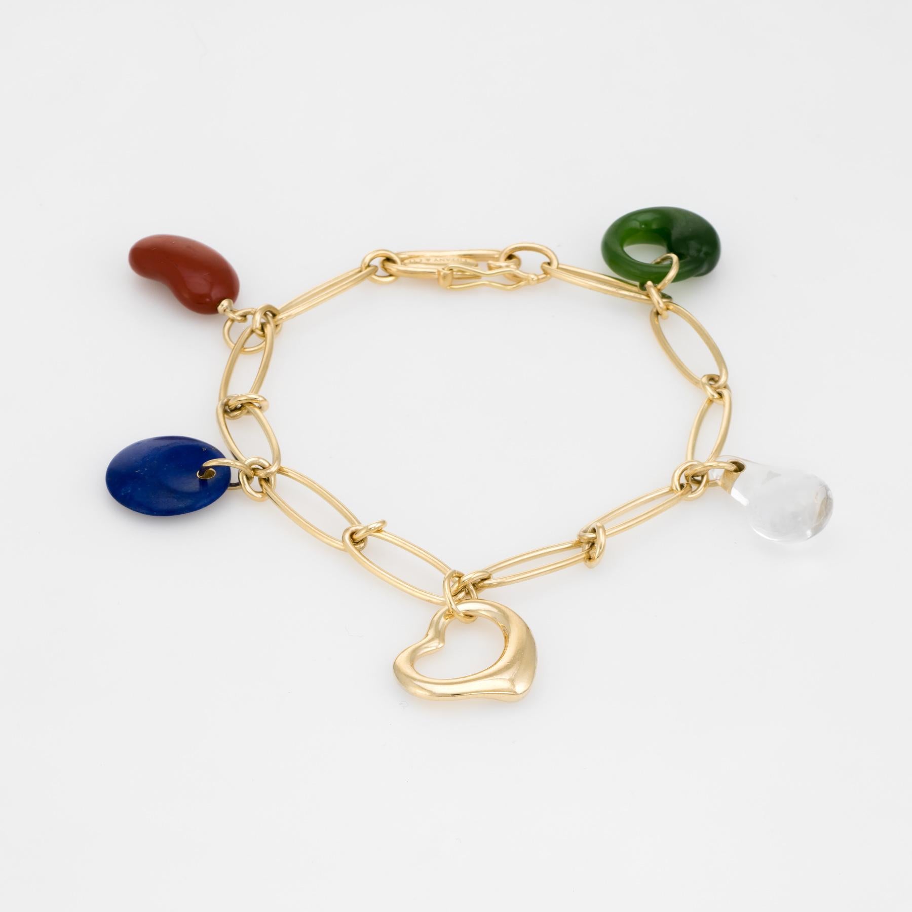 Elegant pre owned Tiffany & Co 5 charm bracelet, crafted in 18k yellow gold. 

The charms are comprised of the following materials: Bean is made of red jasper, the round disc is lapis lazuli, the teardrop is rock crystal and the eternal circle is