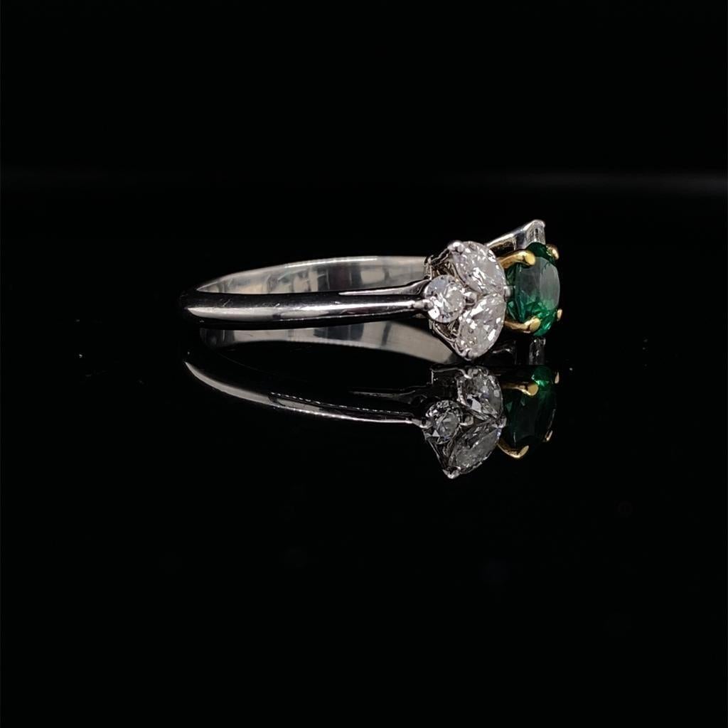 A stunning emerald and diamond engagement ring of floral design set in platinum by Tiffany & Co

The ring is centrally set with a round cut emerald in a simple four claw 18 karat yellow gold setting, which enhances its deep green colour. Elegant