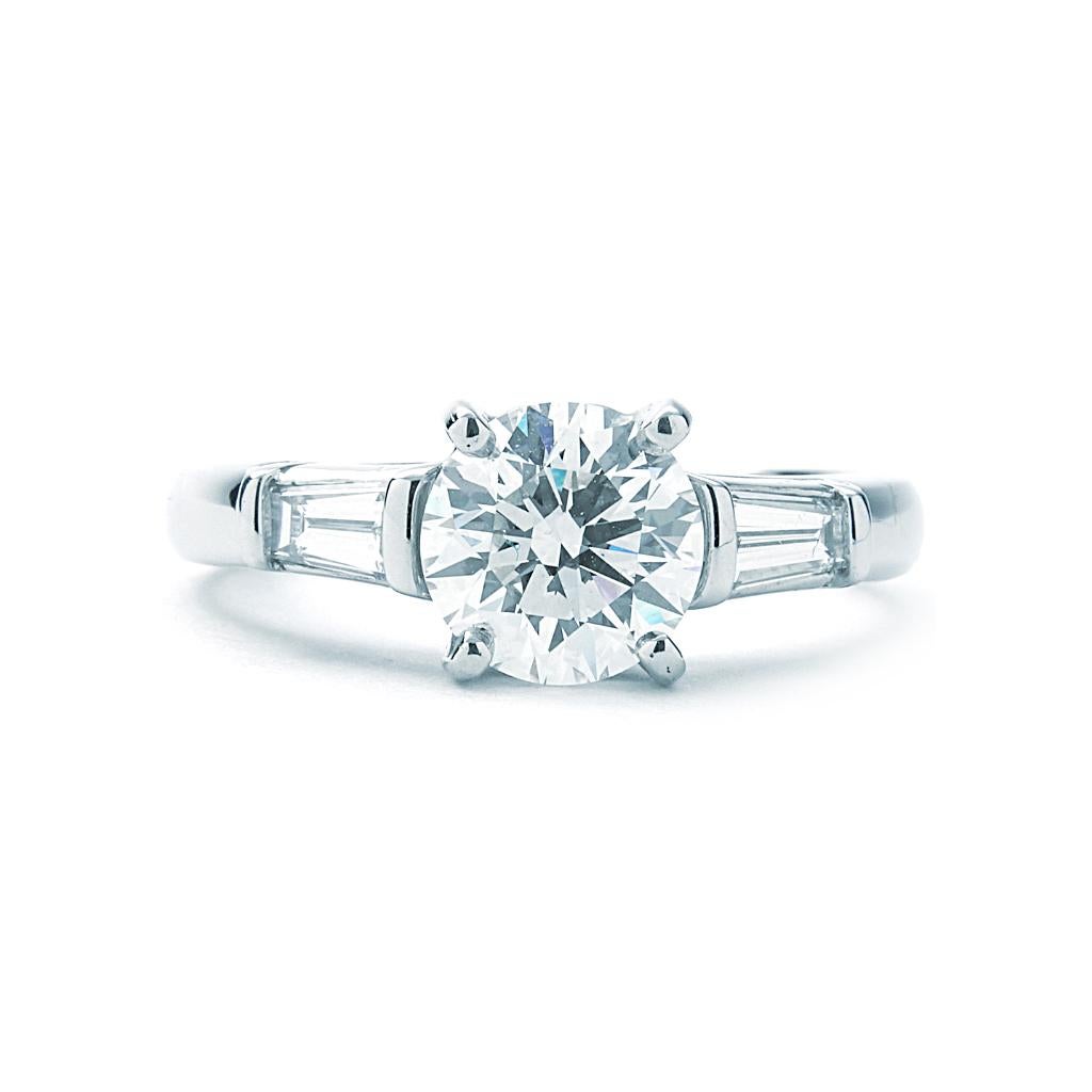 Bague de fiançailles Tiffany & Co. d'occasion. La bague est une taille 6 (US), en platine 950, et pèse 3,8 DWT (environ 5,91 grammes). Elle possède également un diamant rond de couleur G, de pureté VVS2, pesant 1.39 CT, et deux diamants baguette de