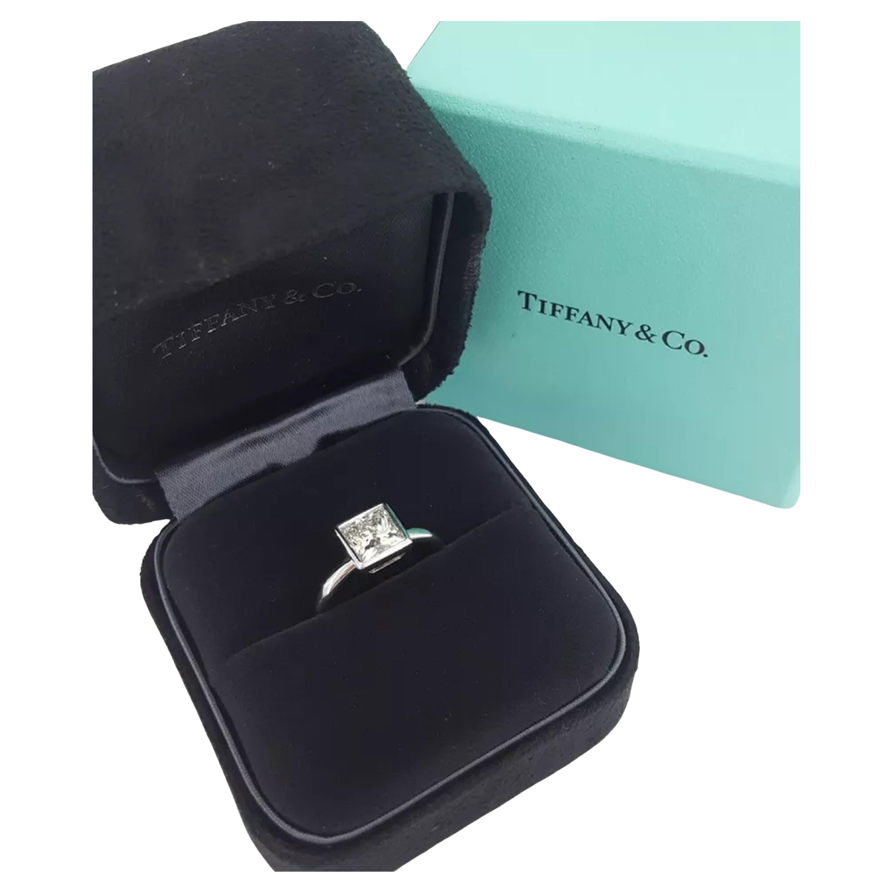 Tiffany & Co. engagement ring features a 2.01 ct Platinum Princess Brilliant Cut diamond set in a bezel setting. The ring weighs 7.7 grams and is a size 5.25. The center stone is a Princess (Square Modified) Brilliant Cut diamond with an H color