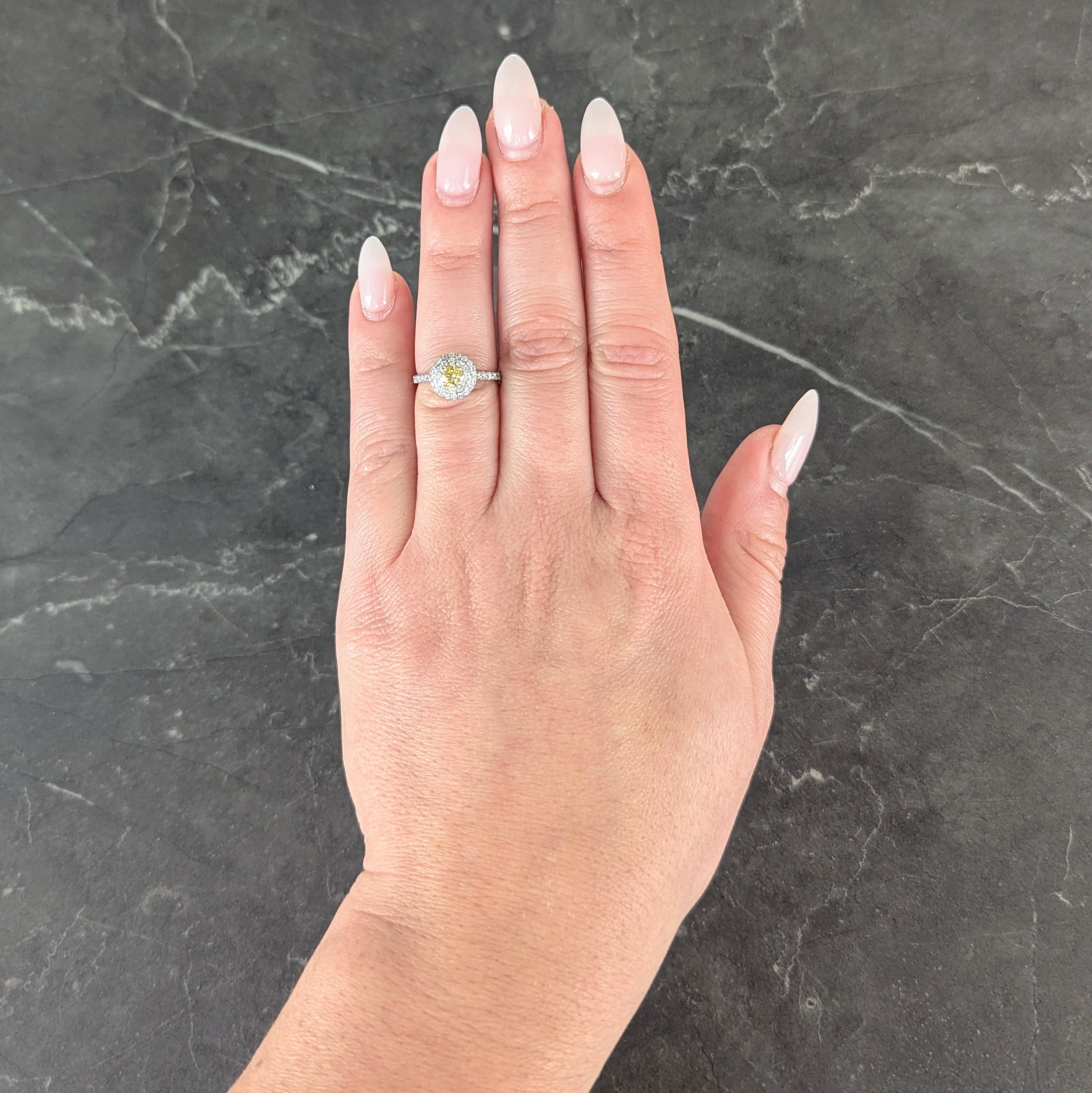 In der Mitte ein runder Diamant im Brillantschliff mit einem Gewicht von 0,20 Karat - fancy vivid yellow mit Reinheit VS2
In Gelbgold gefasst und mit einem doppelten Halo aus Diamanten aus Platin umgeben
Mit zusätzlichen Diamanten, die in Zacken auf