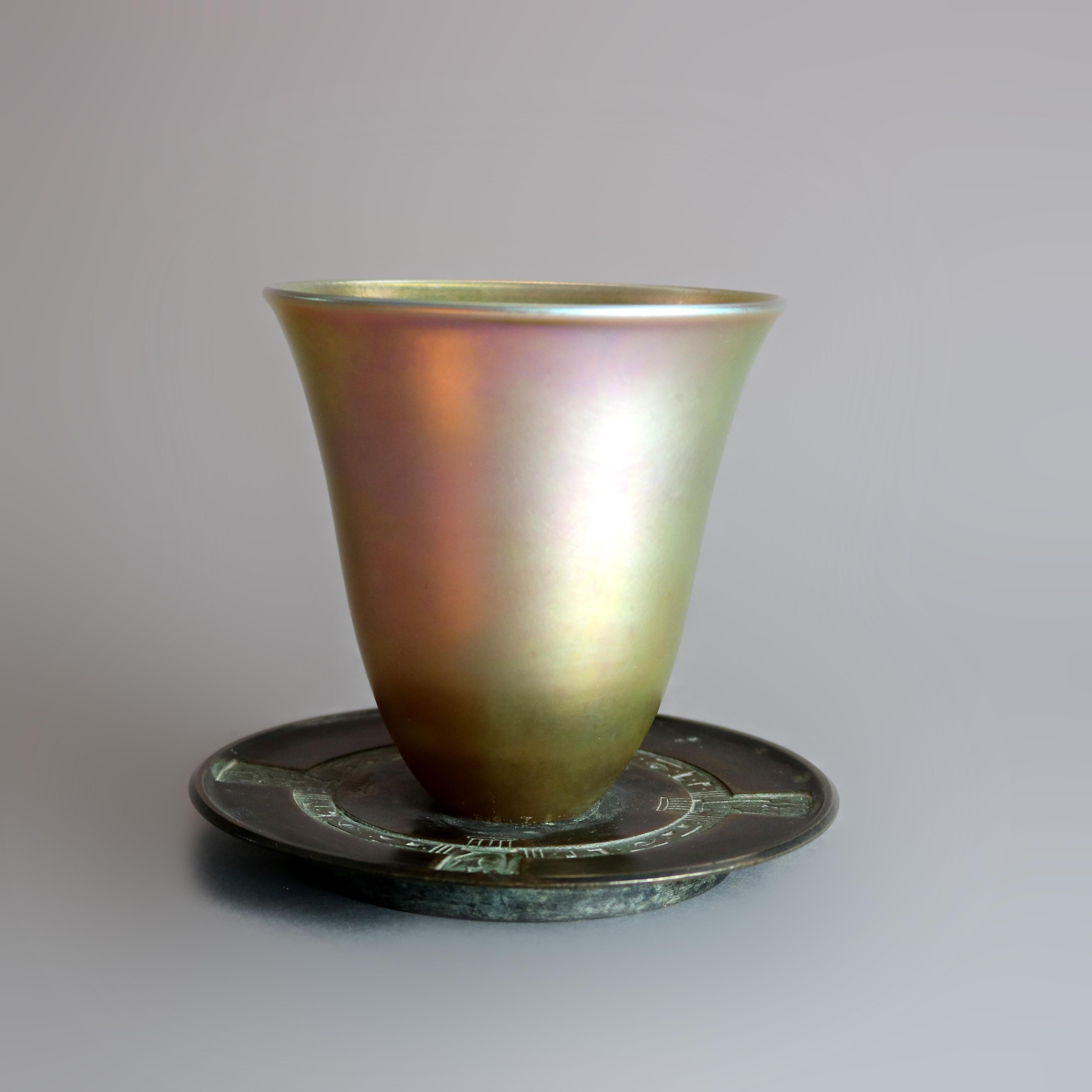 An antique Egyptian Revival libation cup by Tiffany & Co. offers flared Favrile art glass vessel seated on cast bronze base with repeating design having symbols and stylized figures, stamped on base as photographed, circa 1890

Measures: 4.5