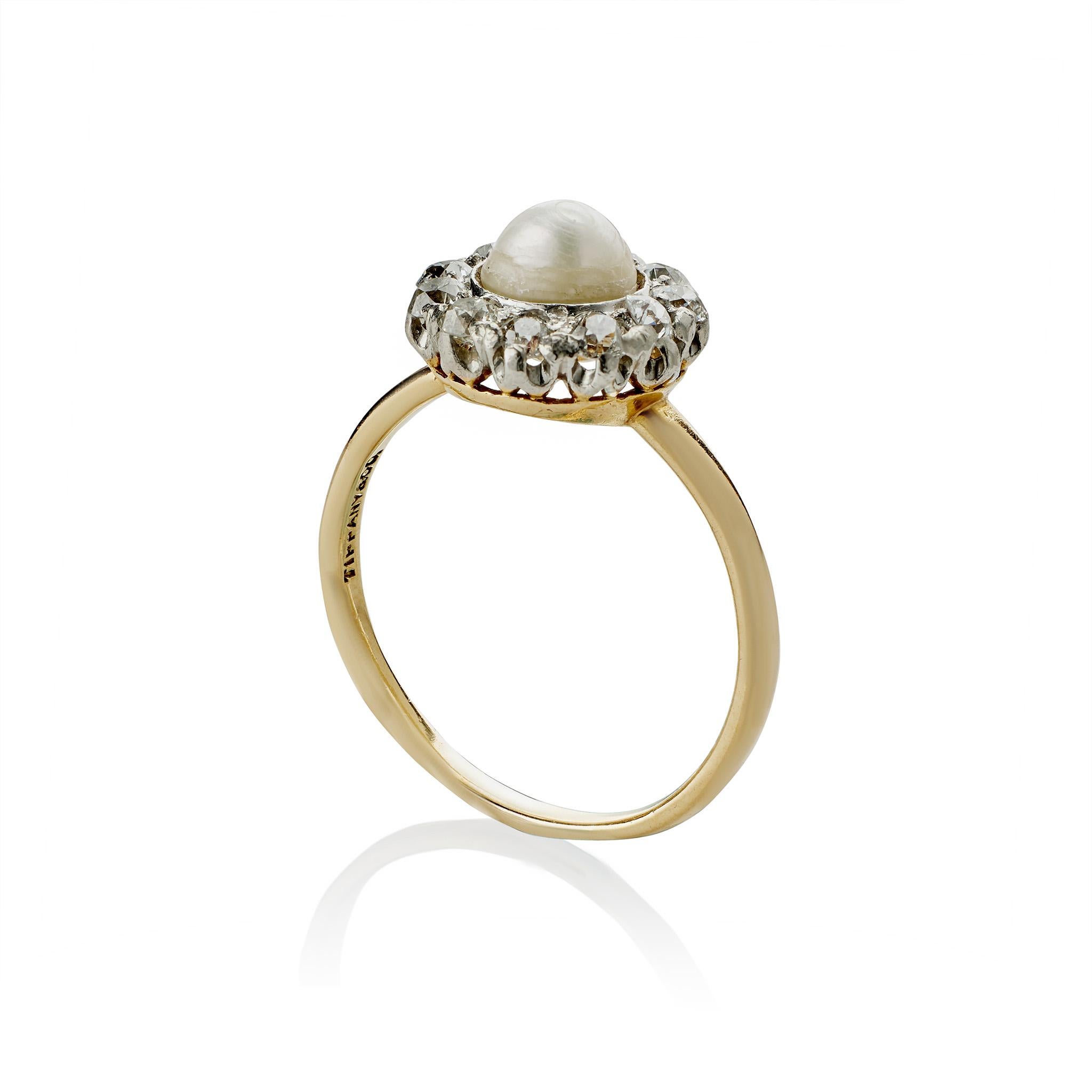 Dating to circa 1900, this Tiffany & Co. ring is set with a freshwater pearl and diamonds. The ring centers a high domed button pearl with ivory tones, framed by eleven old European-cut diamonds, mounted in platinum-topped 18K gold. This refined and